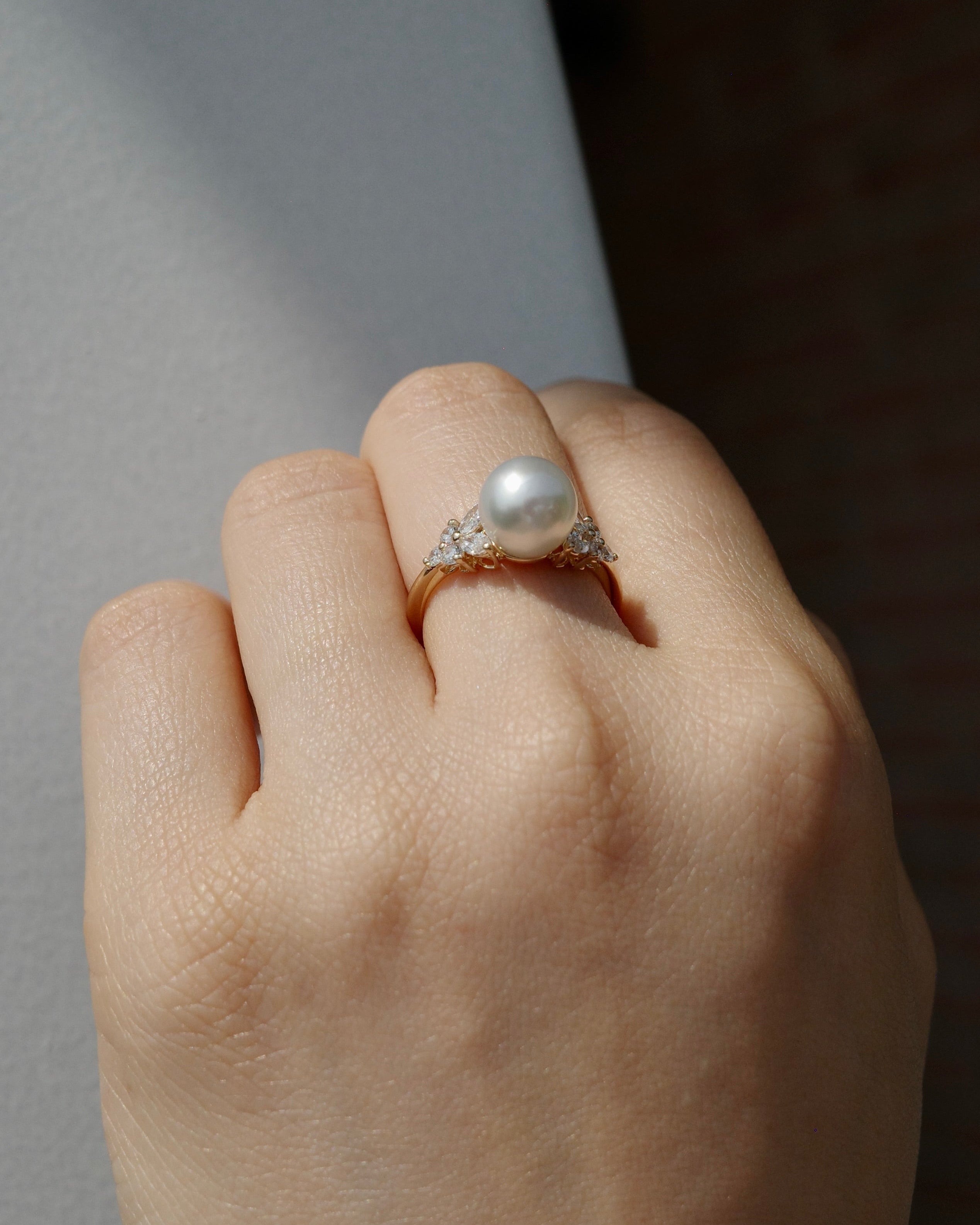 Hand wearing a south sea round pearl and marquise diamonds ring on a neutral background