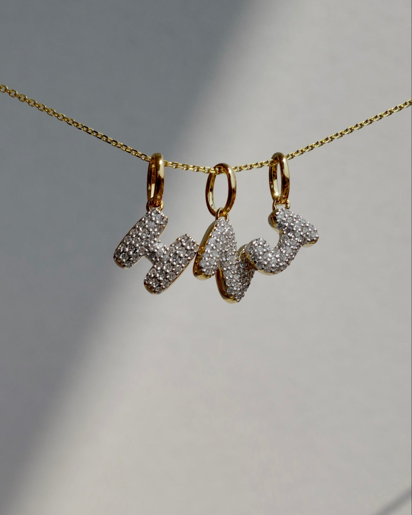 Gold necklace with 'HNJ' charms on a neutral background