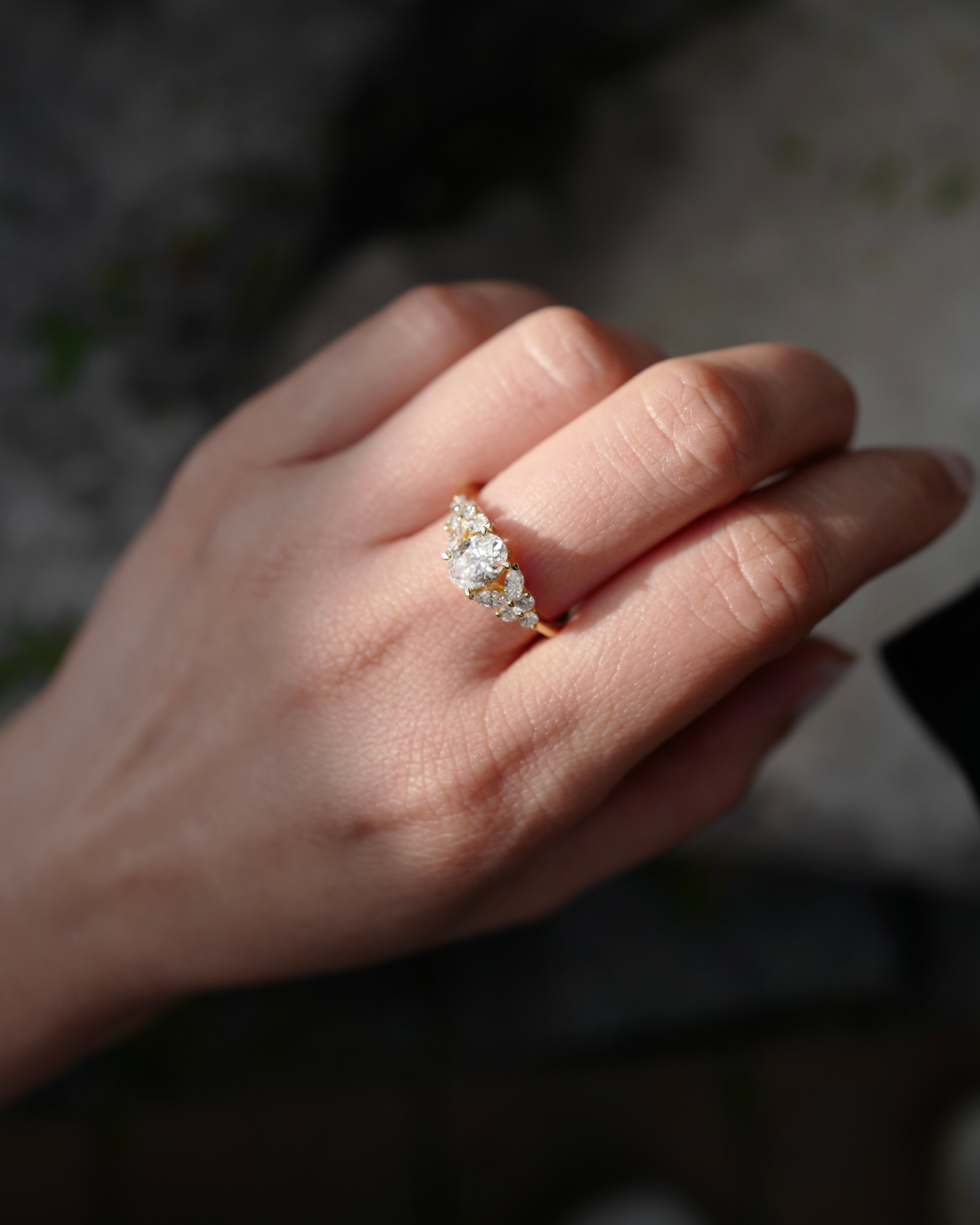 Hand wearing a oval diamond and marquise diamond ring with a natural light background