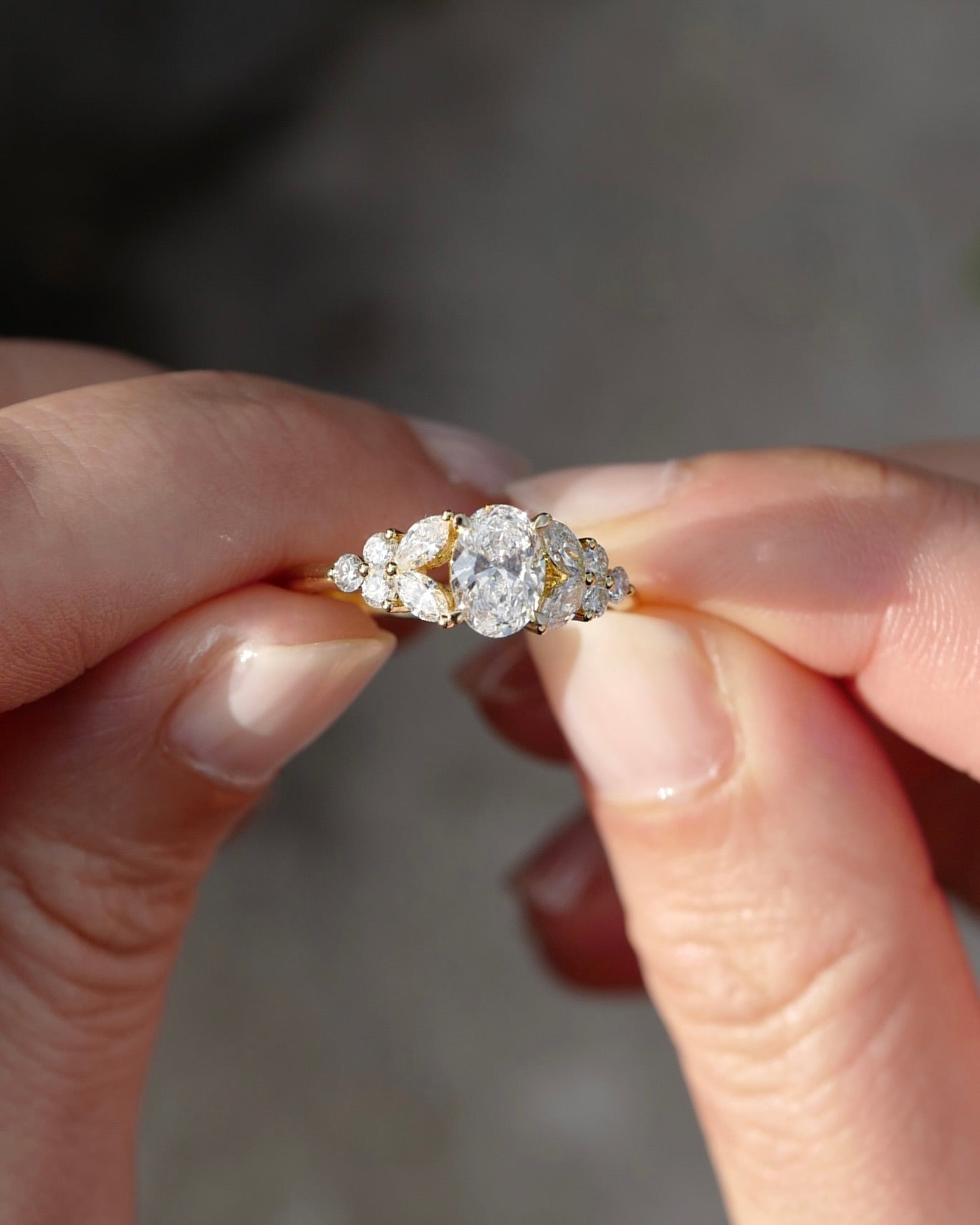 An oval diamond gold ring held between fingers against a blurred background