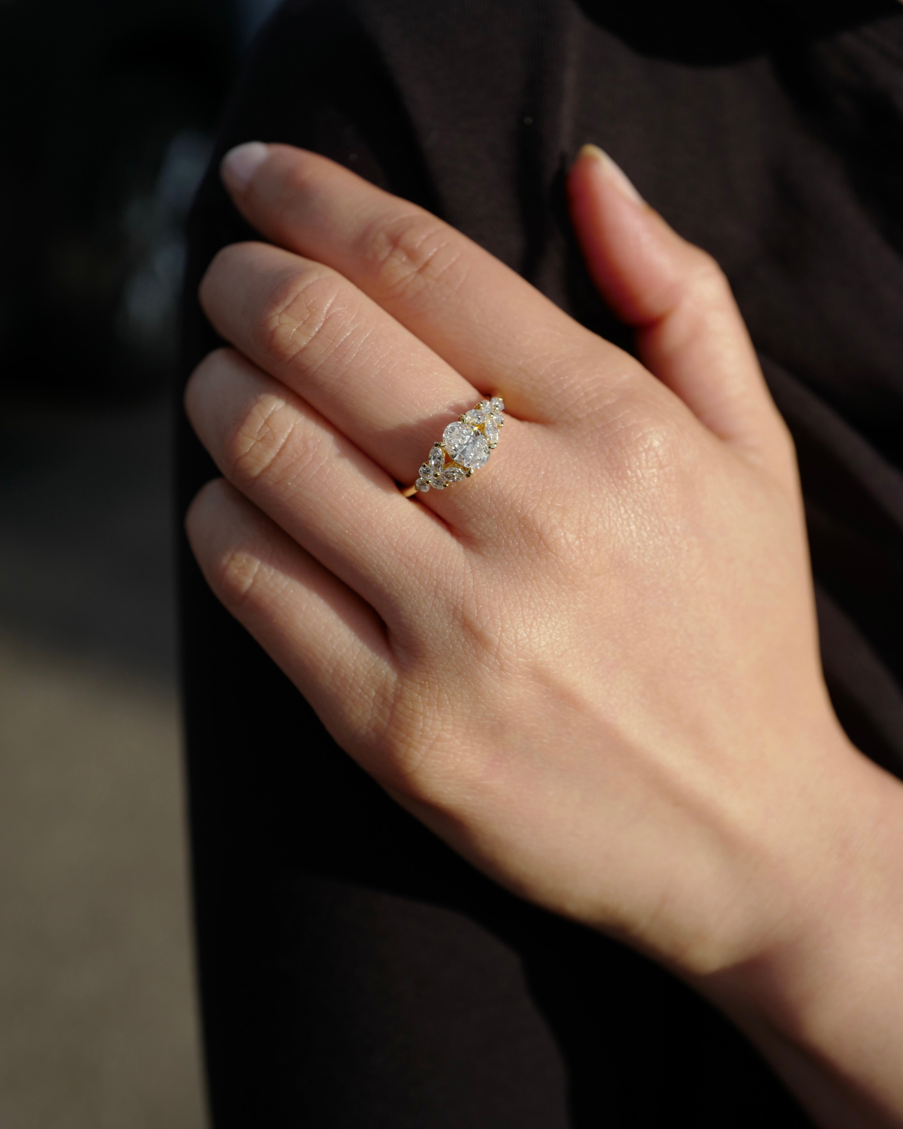 Hand wearing an engagement ring with an oval diamond at the center along with marquise diamonds and round brilliant cut diamonds on the side