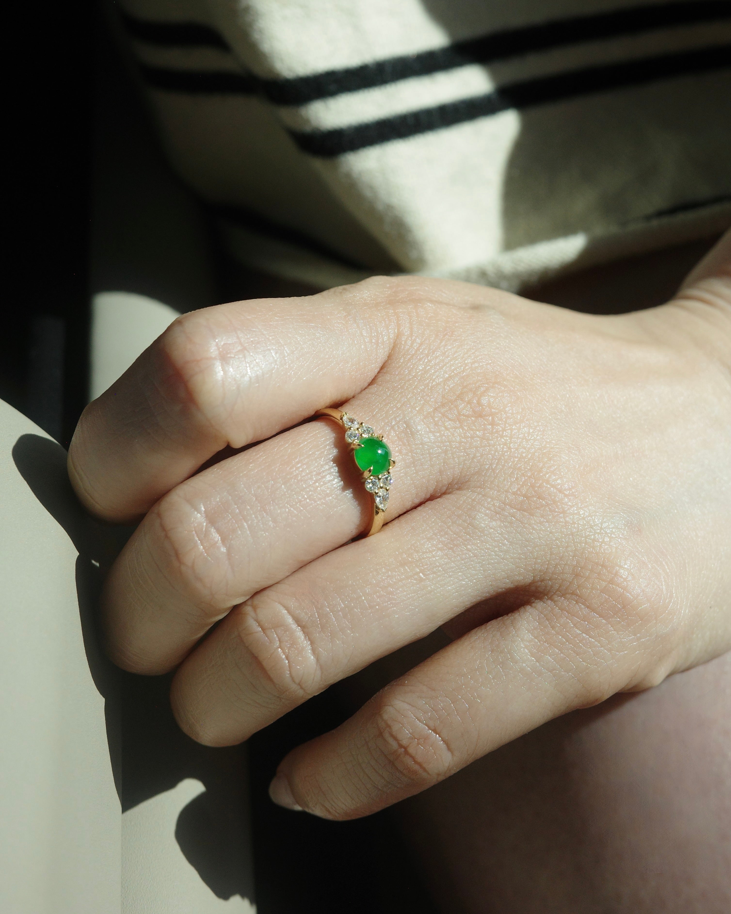 Hand wearing a ring with a 5mm round jade at the center along with pear diamonds and round brilliant cut diamonds on the side.