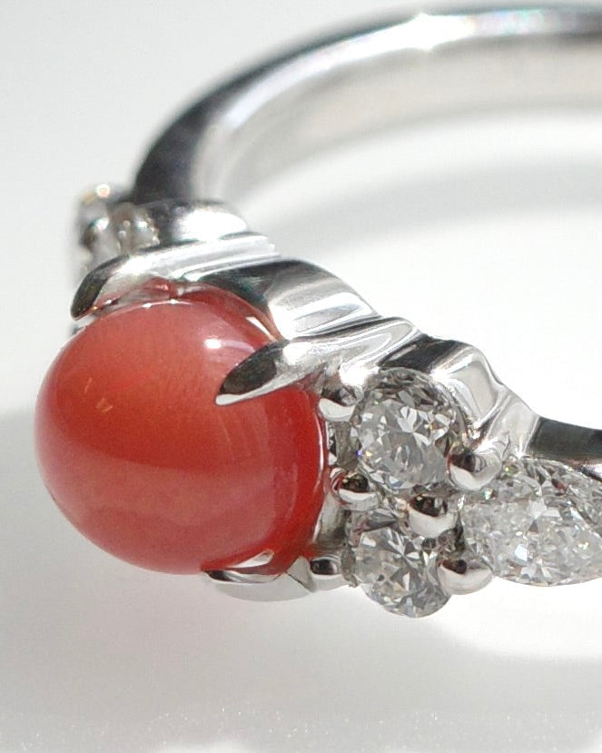 A white gold ring featuring a round, red natural conch pearl and pear diamonds and round brilliant cut diamonds, shown on a white background.