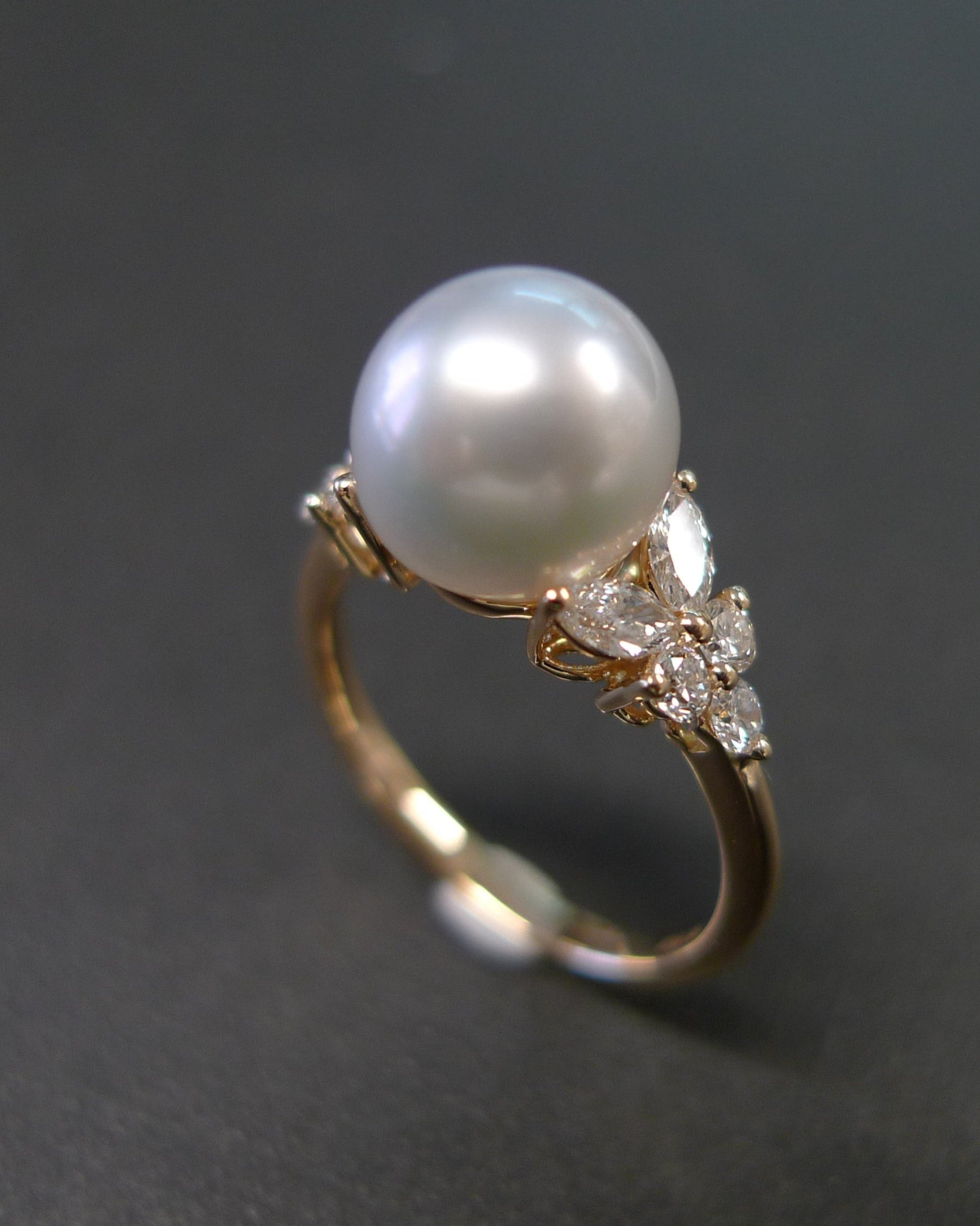 Pearl ring with gold band and diamond accents on a dark background