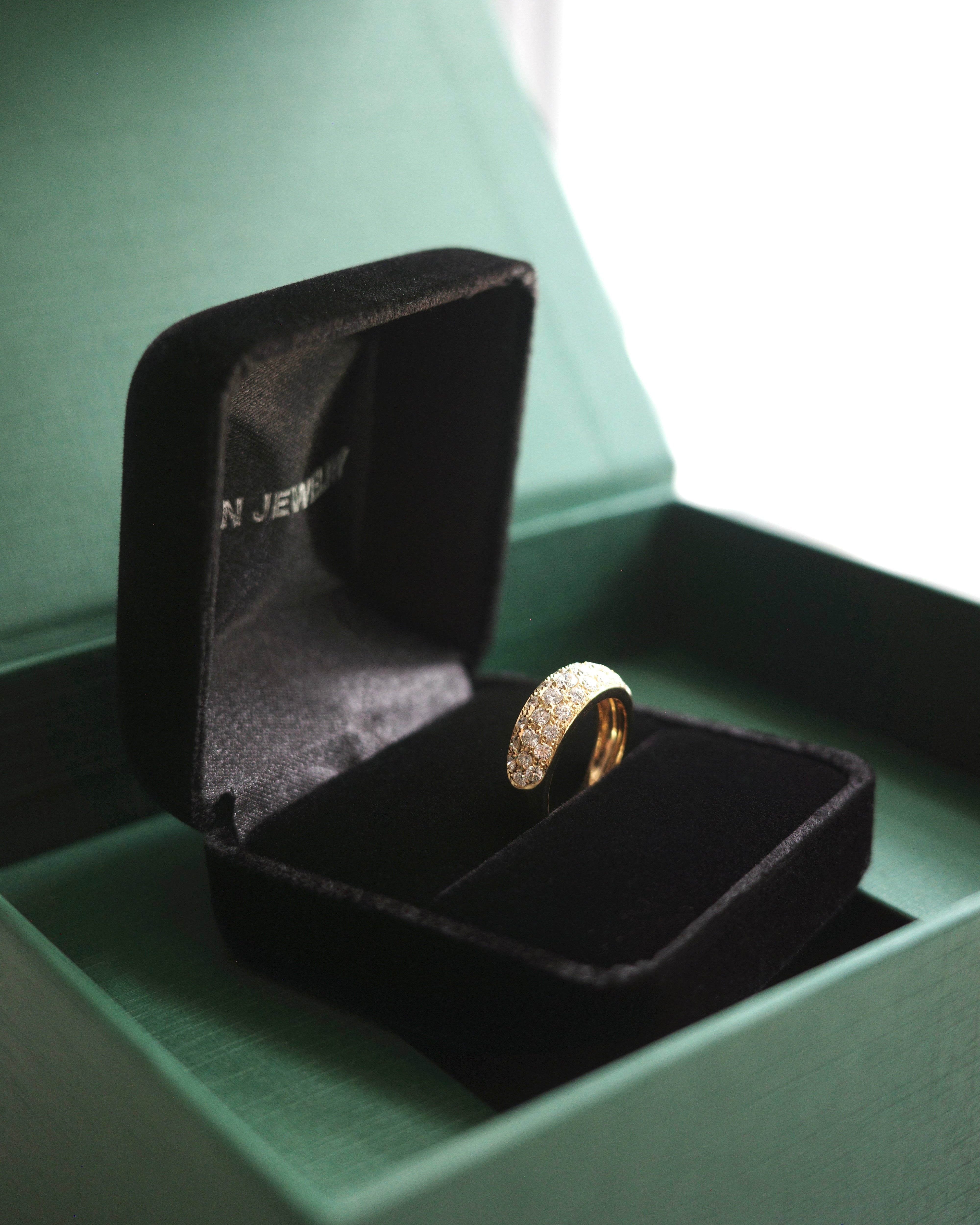 Gold diamond wide ring in a black ring box with 'HN Jewelry' branding on a green packaging box