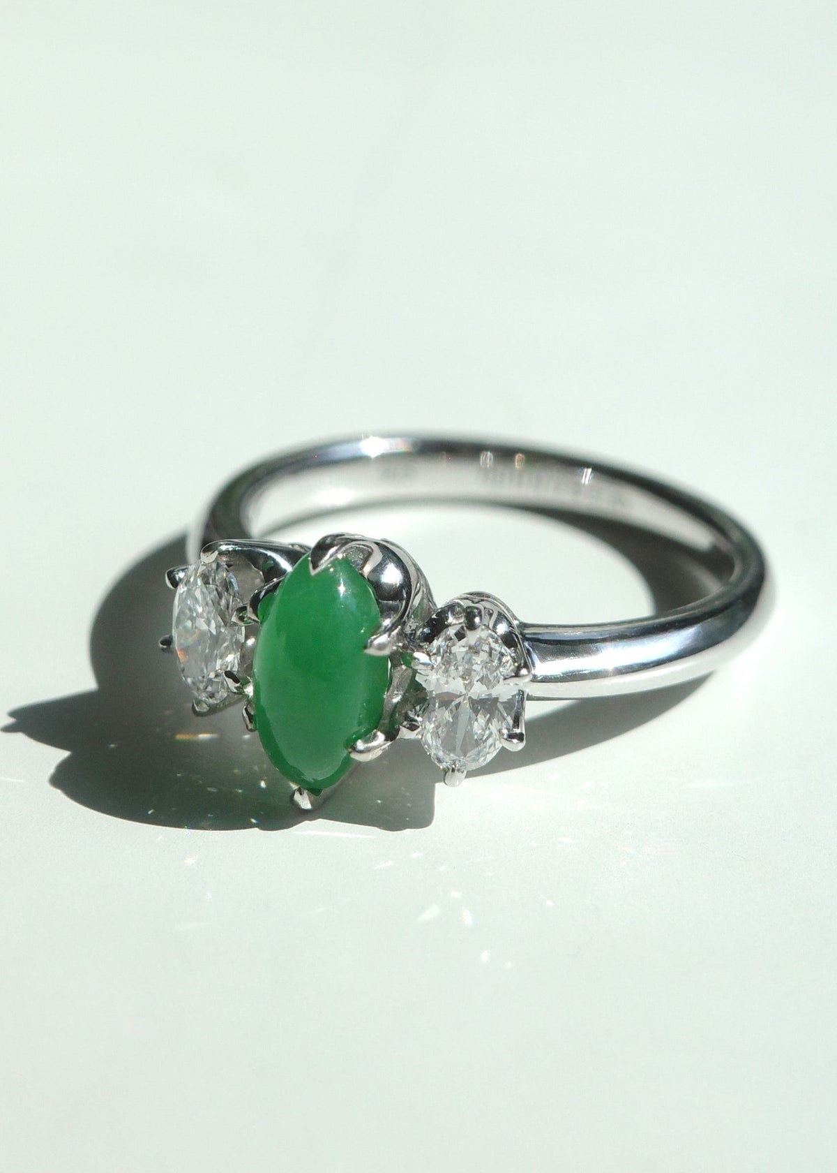 Angle view of a three stone marquise green jadeite ring in solid 14k white gold, highlighting the secure prong settings and brilliant oval side diamonds.