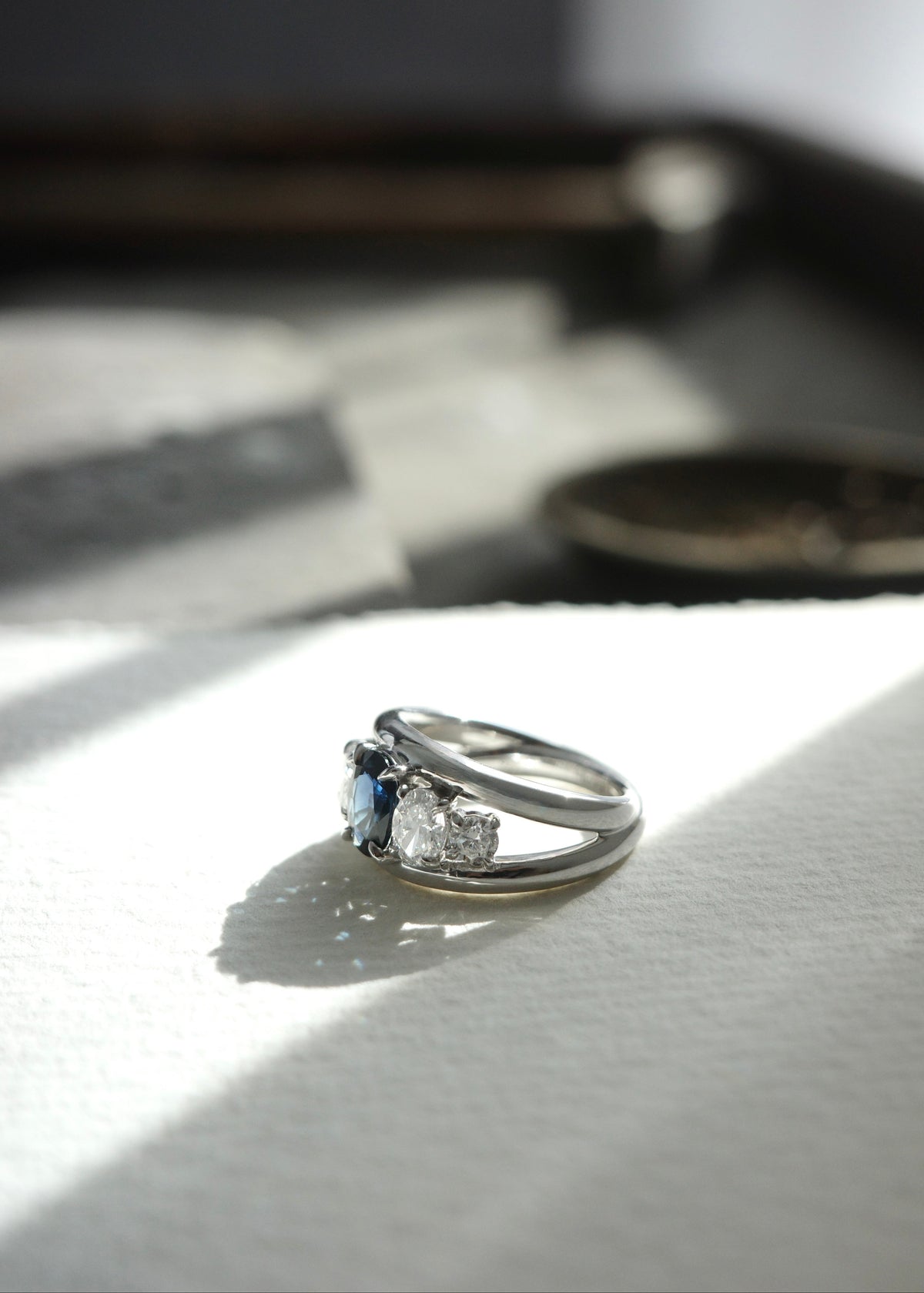 Side view of ocean blue-green teal sapphire ring showing oval and round accent diamonds on white gold band.