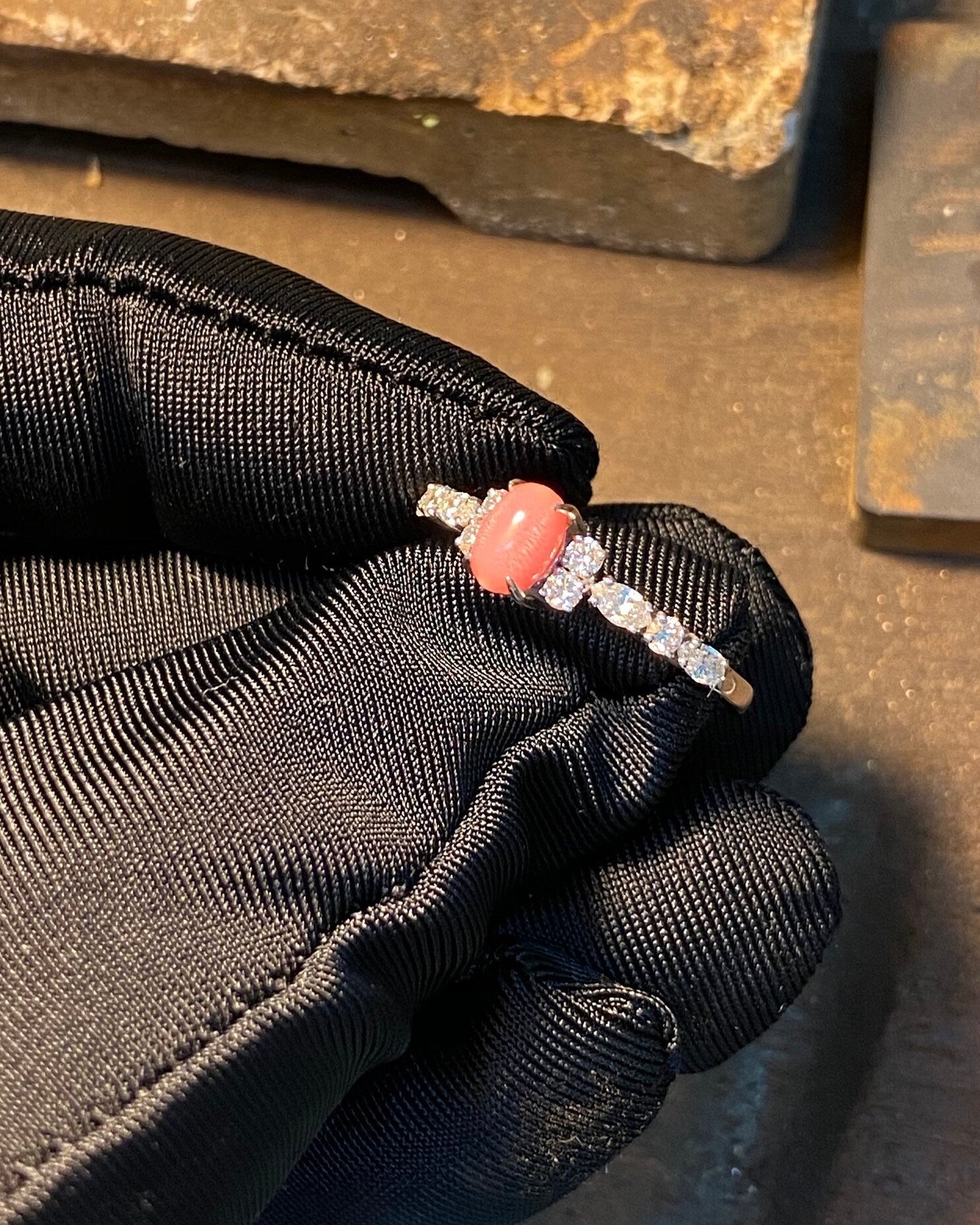 Black glove holding a silver ring with a red stone against a rusty metal background