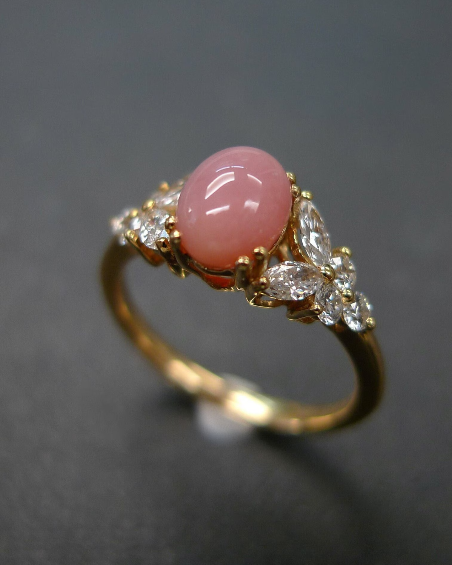 Gold ring with a pink gemstone and diamond accents on a dark background