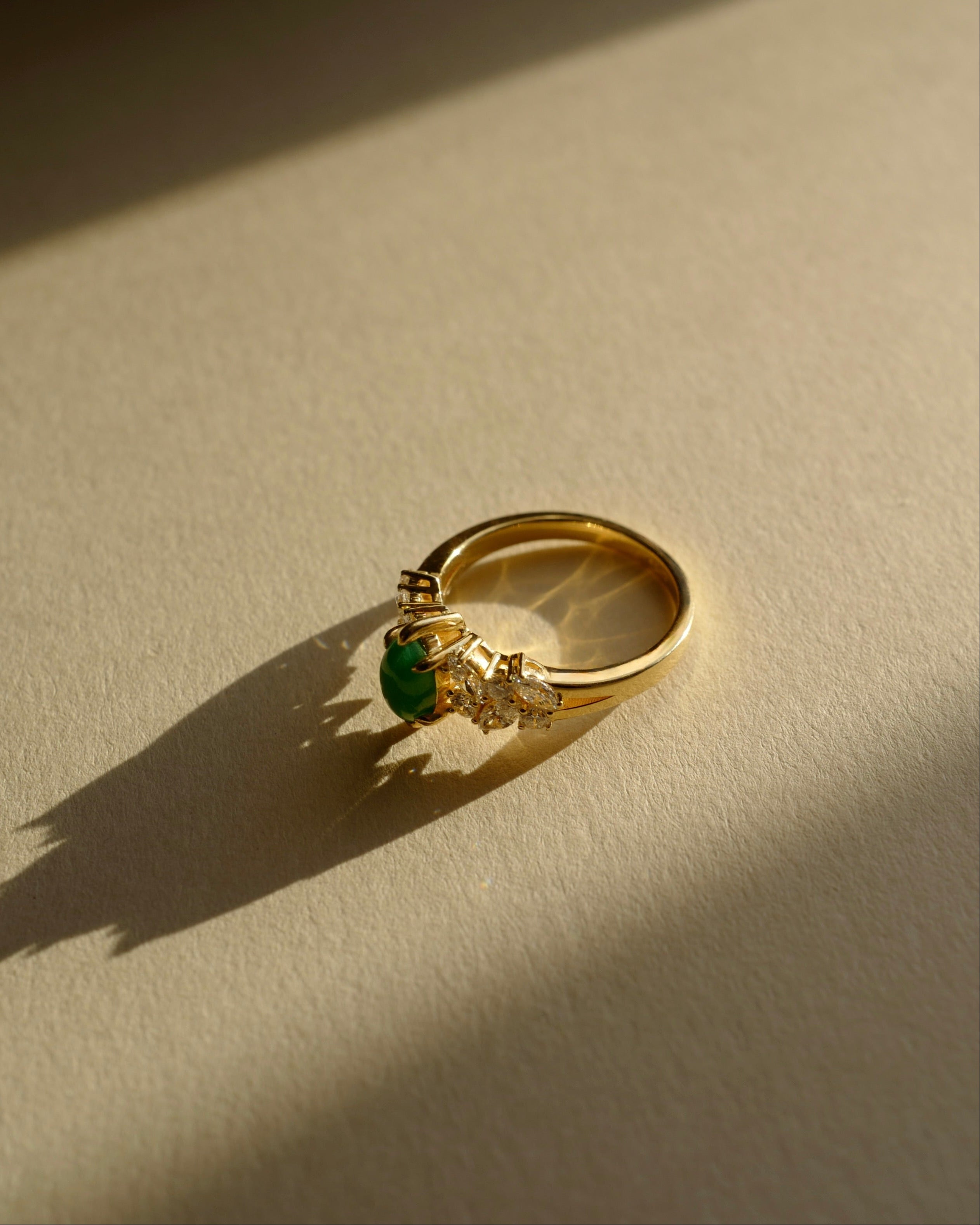 14k solid Gold engagement ring with a green jade and marquise diamond on a beige surface