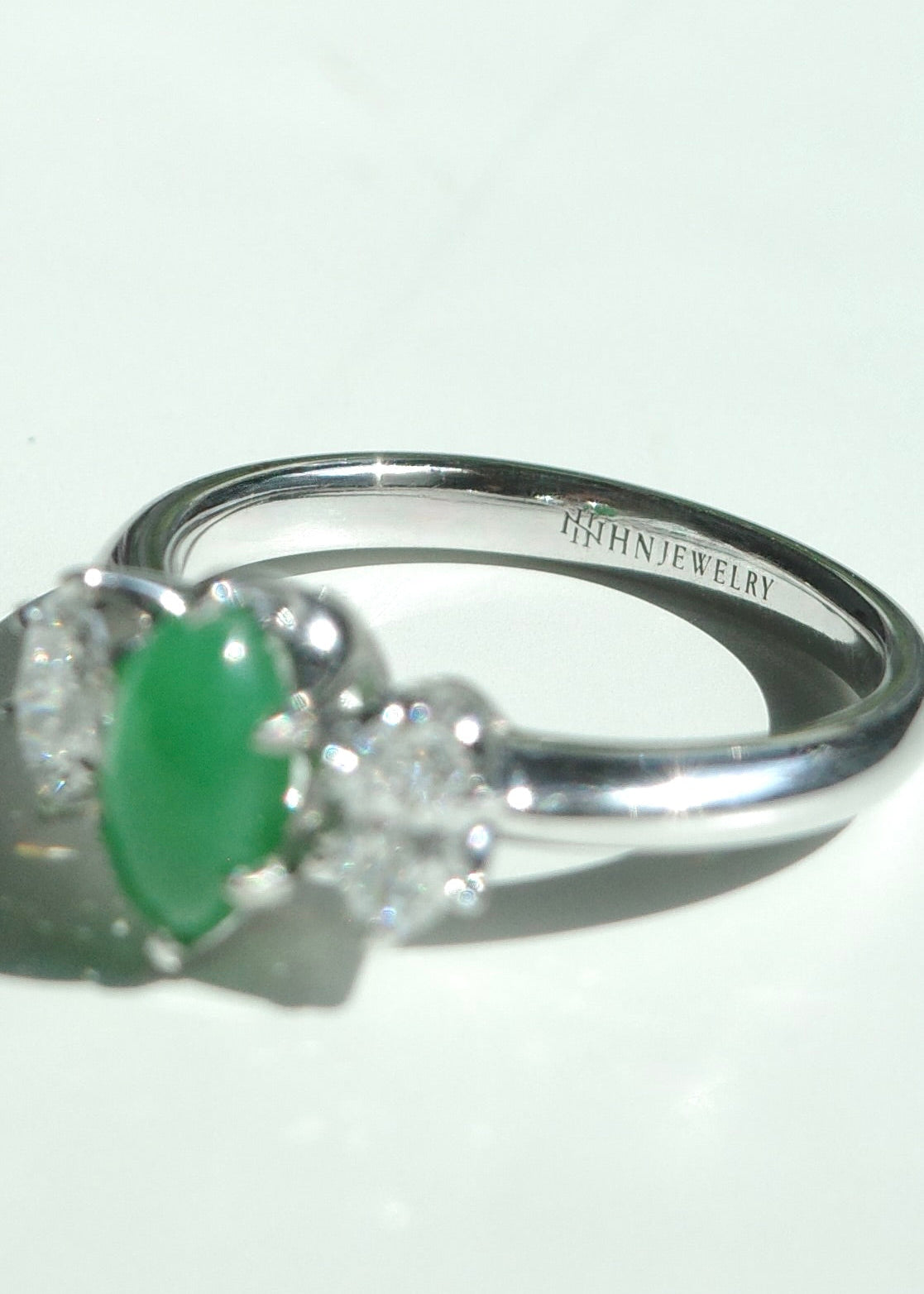 Macro close-up shot of a polished 14k white gold band showing the HN Jewelry brand hallmark engraving near the three stone jade setting.