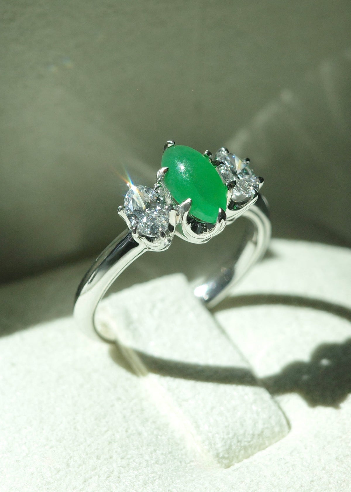 Top view detailed macro shot of a three stone green jadeite marquise ring on display, showing the sleek 14k white gold band and diamond cluster symmetry.