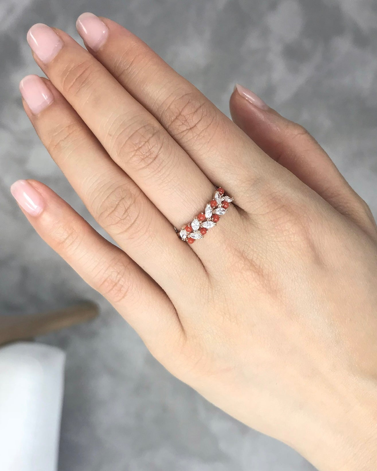 Hand wearing a ring with natural coral and marquise diamond on a neutral background