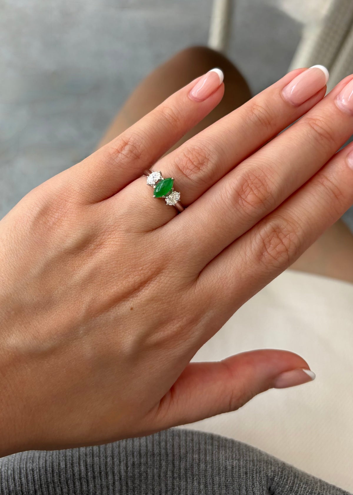 Natural marquise green jade three stone ring worn on hand in sunlight, flanked by icy oval diamonds in a polished 14k white gold setting.