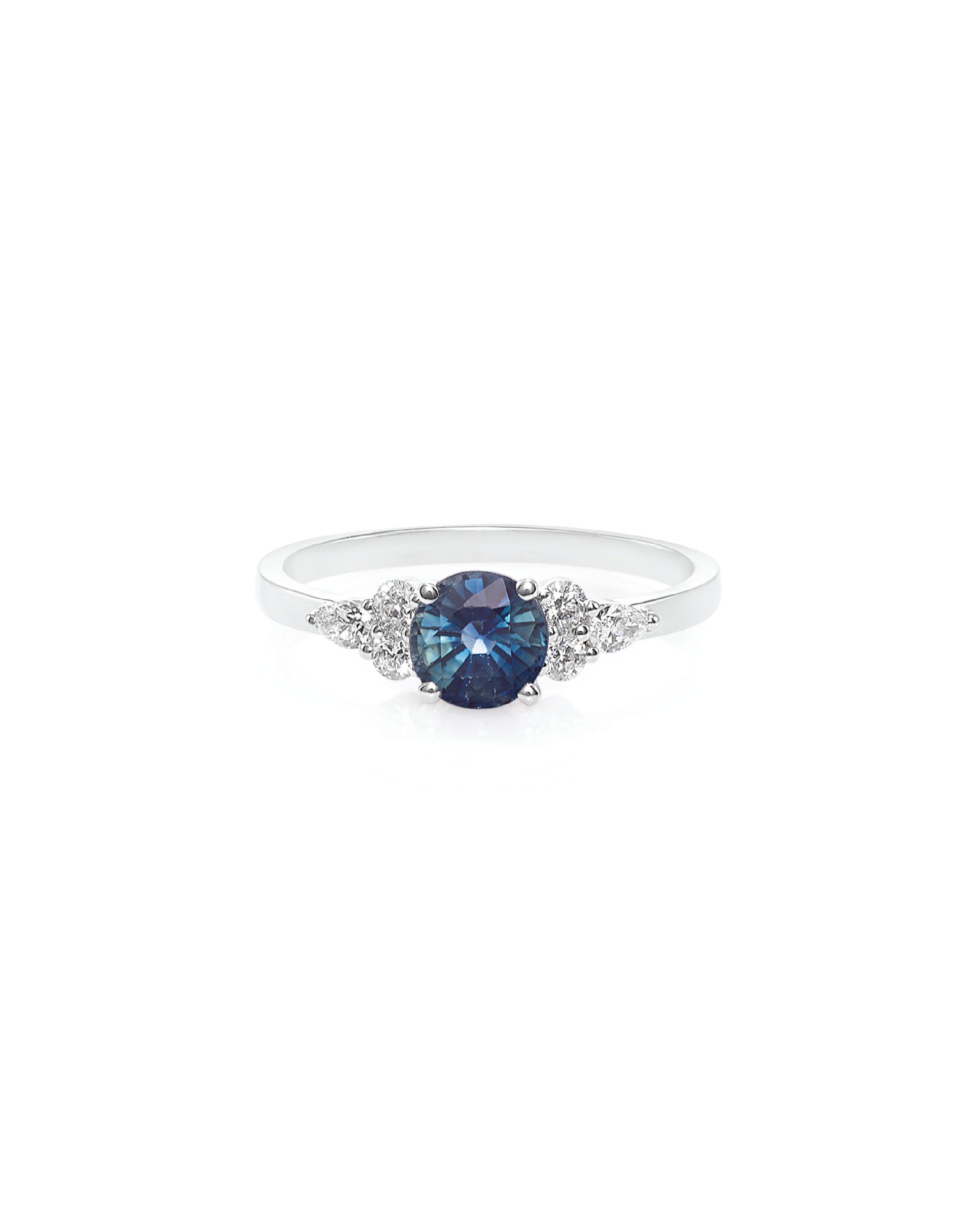 A ring featuring a round teal sapphire center stone with round and pear cut diamonds flanking on either side, set in 14K white gold.