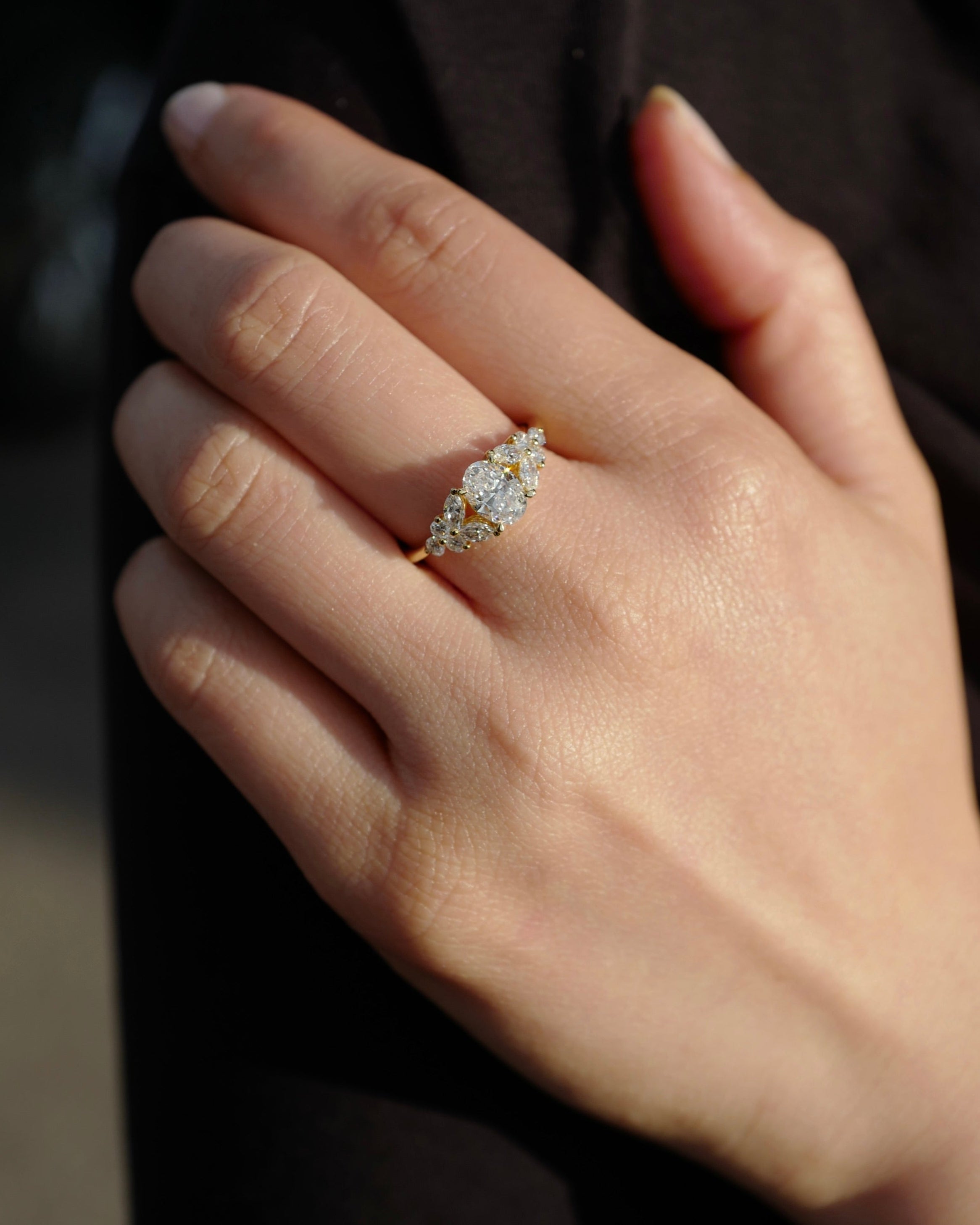 Hand wearing an engagement ring with an oval diamond at the center along with marquise diamonds and round brilliant cut diamonds on the side