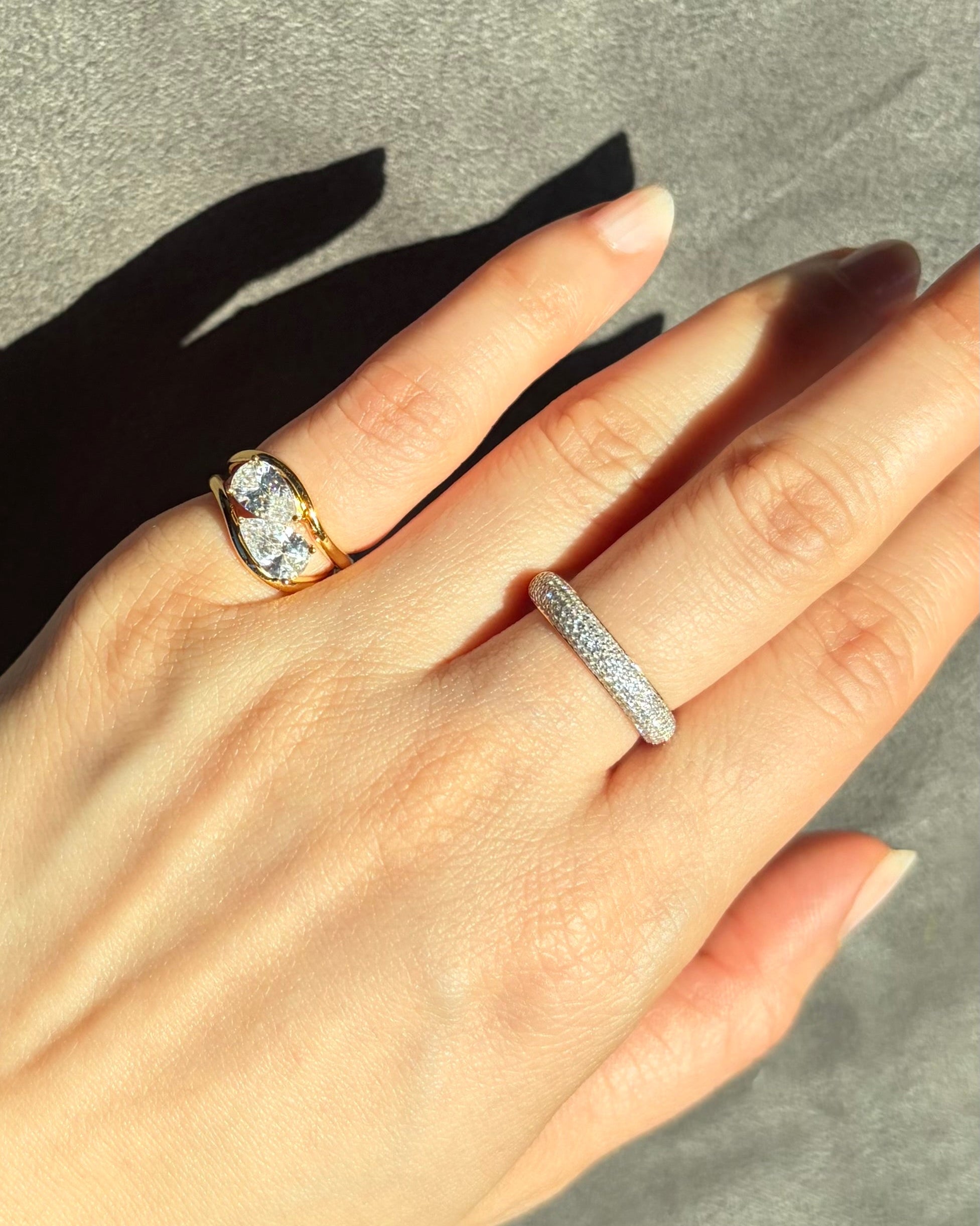 Hand wearing two pinky rings with a gray background