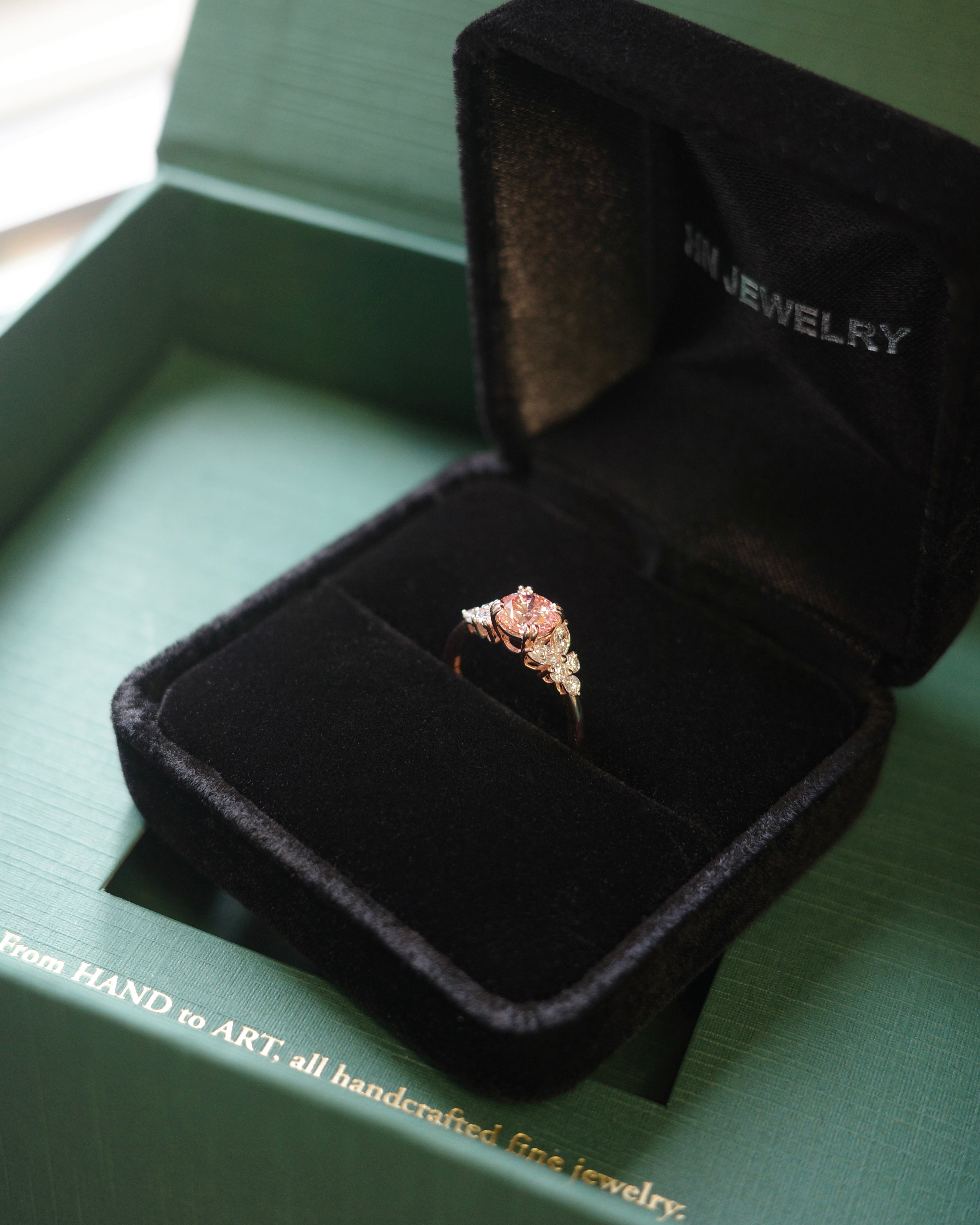 Jewelry box with a pink diamond ring inside on a green packaging
