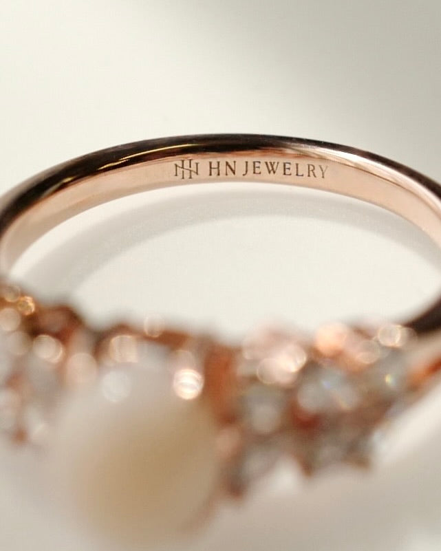 Close-up of a rose gold ring band engraved with 'HN JEWELRY' and a HN Jewelry logo, with a soft-focus view of the setting below.