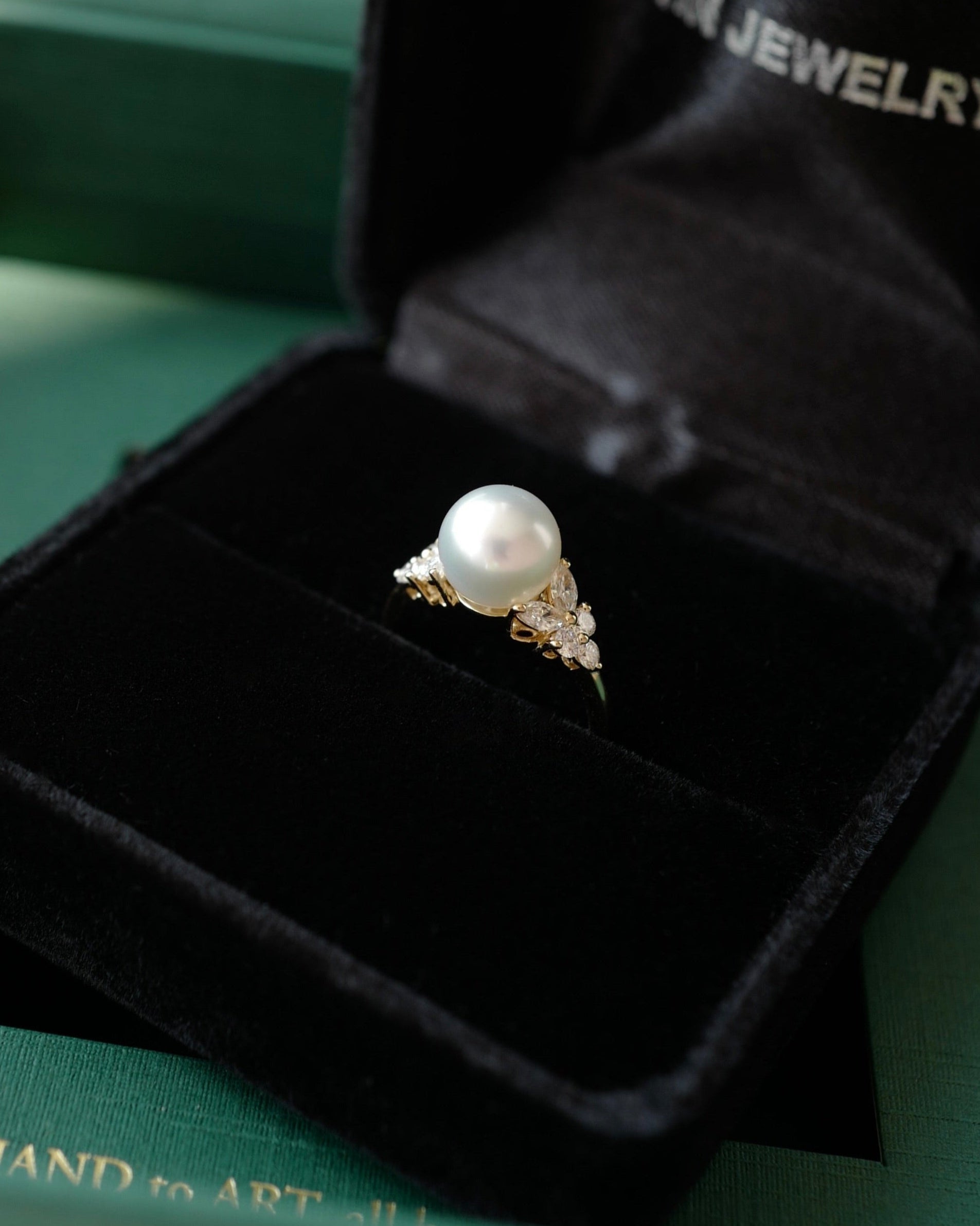 Pearl ring in a black jewelry box with HN Jewelry branding on a green background