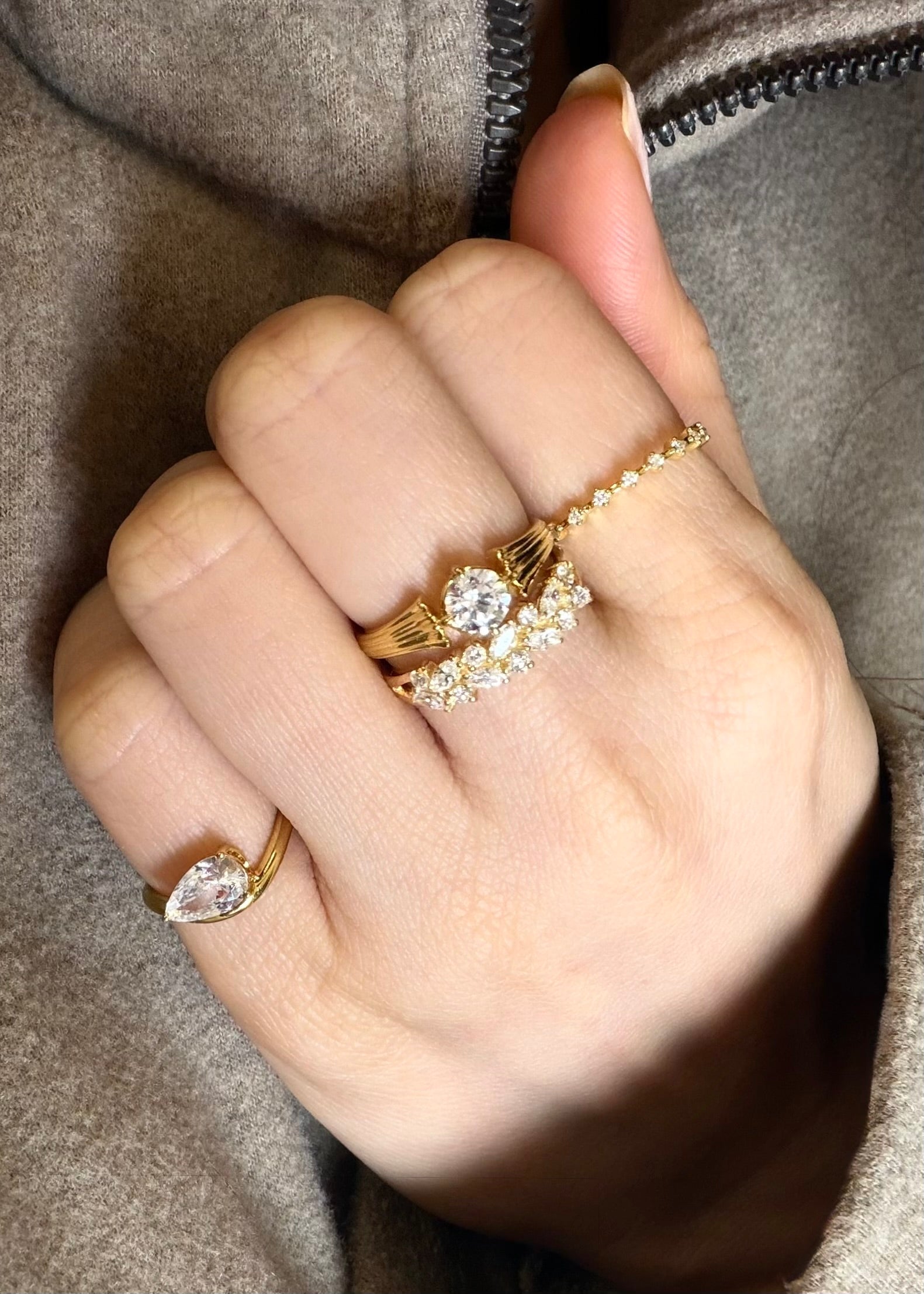Hand wearing gold rings with diamond accents against a neutral background