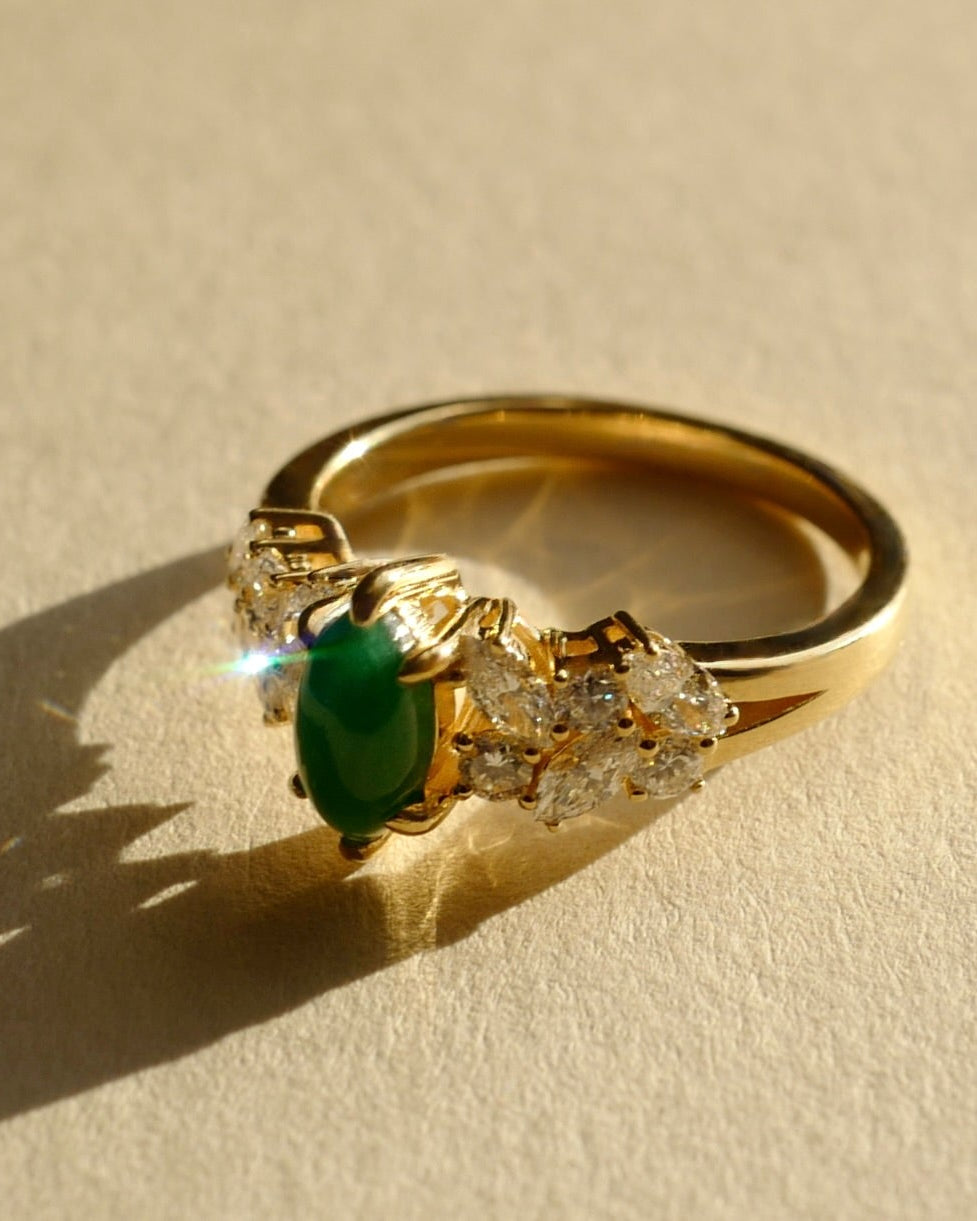 Gold ring with a natural green jade and diamond accents on a beige background