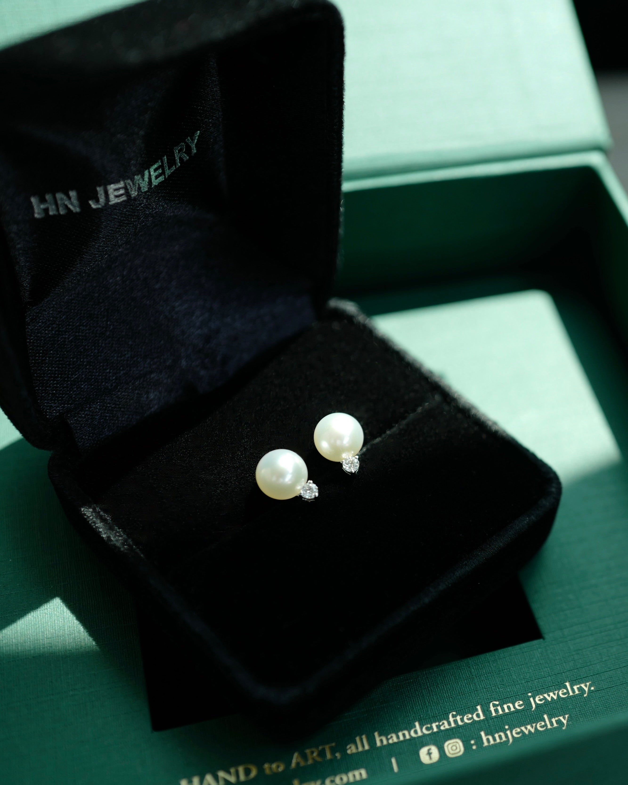 Pearl earrings in a black jewelry box on a green HN Jewelry branded box.