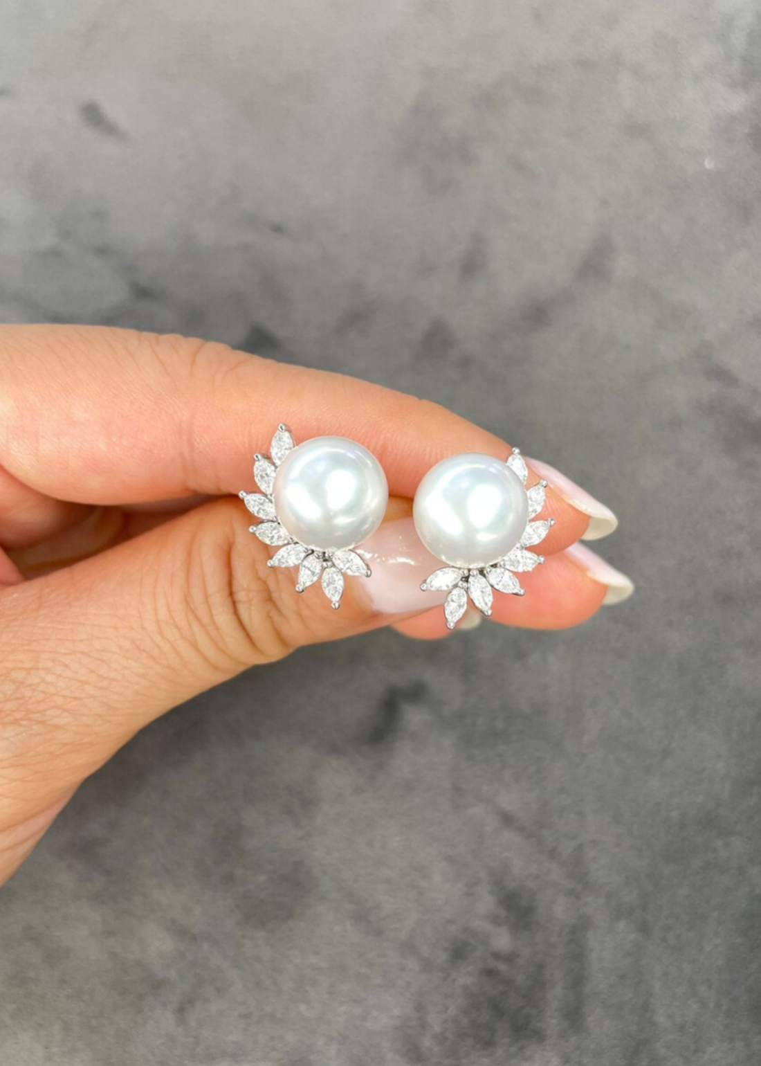 Pearl earrings with silver accents held by a hand against a gray background