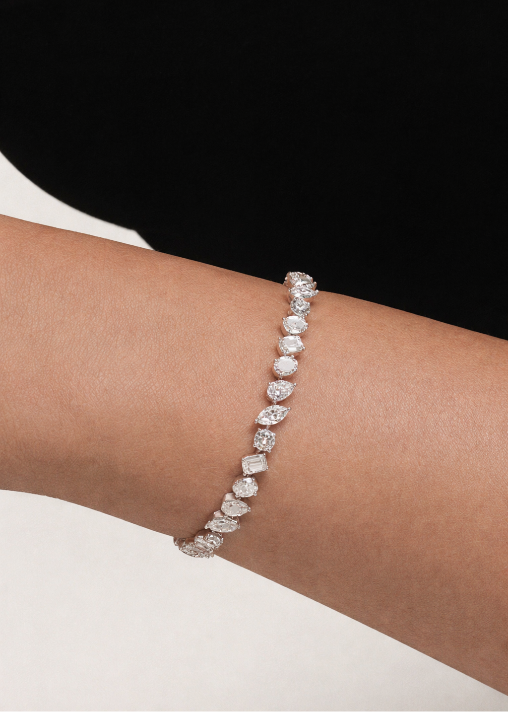 white gold bracelet with multi shape diamonds on a person's wrist against a black background