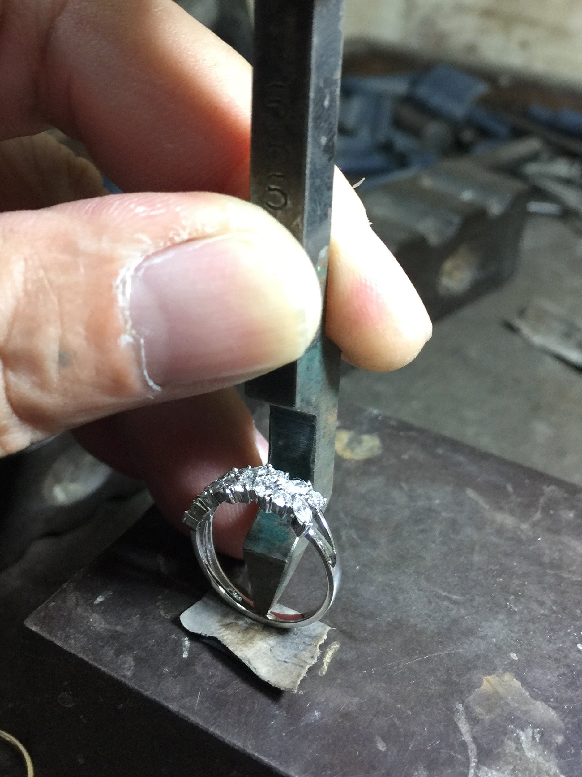 A jeweler is Hand stamping HN Jewelry logo inside a ring with a metal tool on a workshop background 