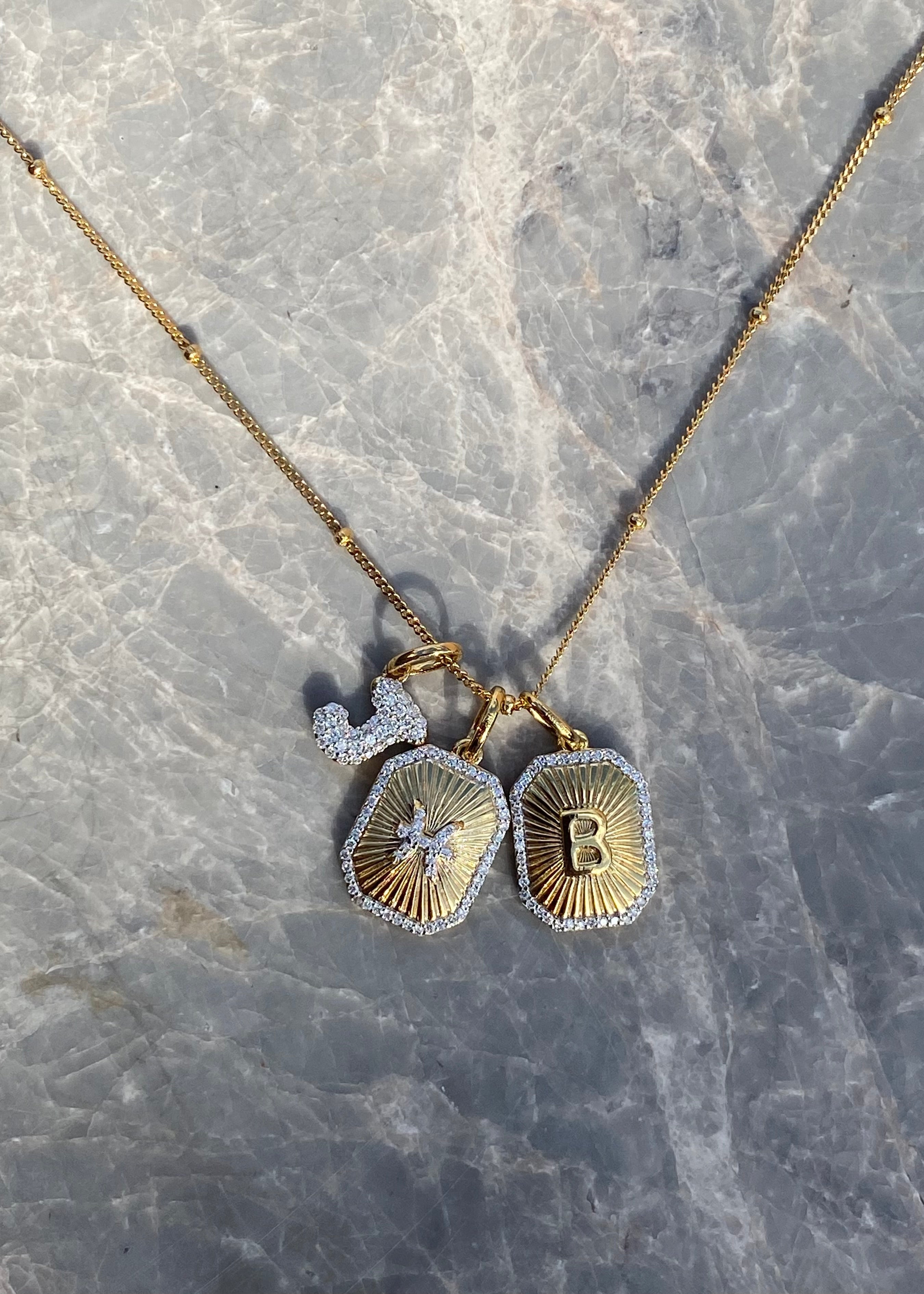 Gold necklace with two pendants on a marble surface