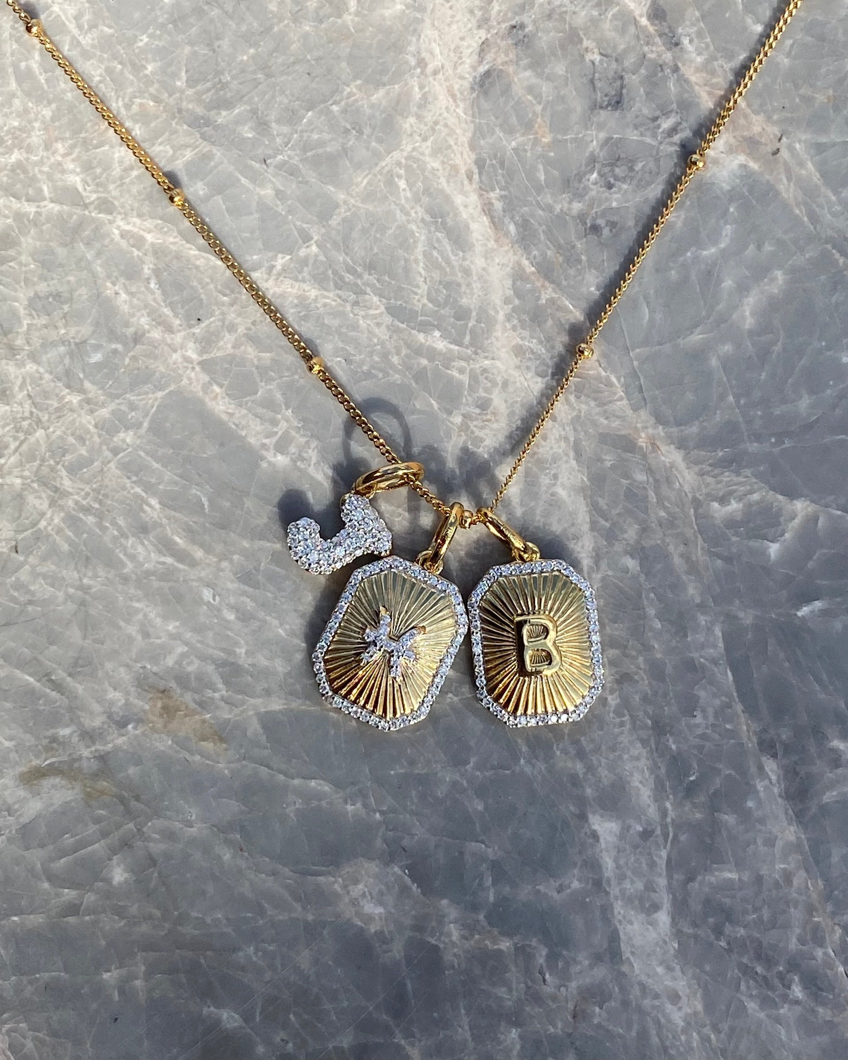 Gold necklace with two pendants on a marble surface