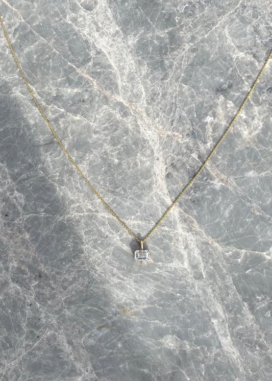 Gold necklace with a small square pendant on a marble surface