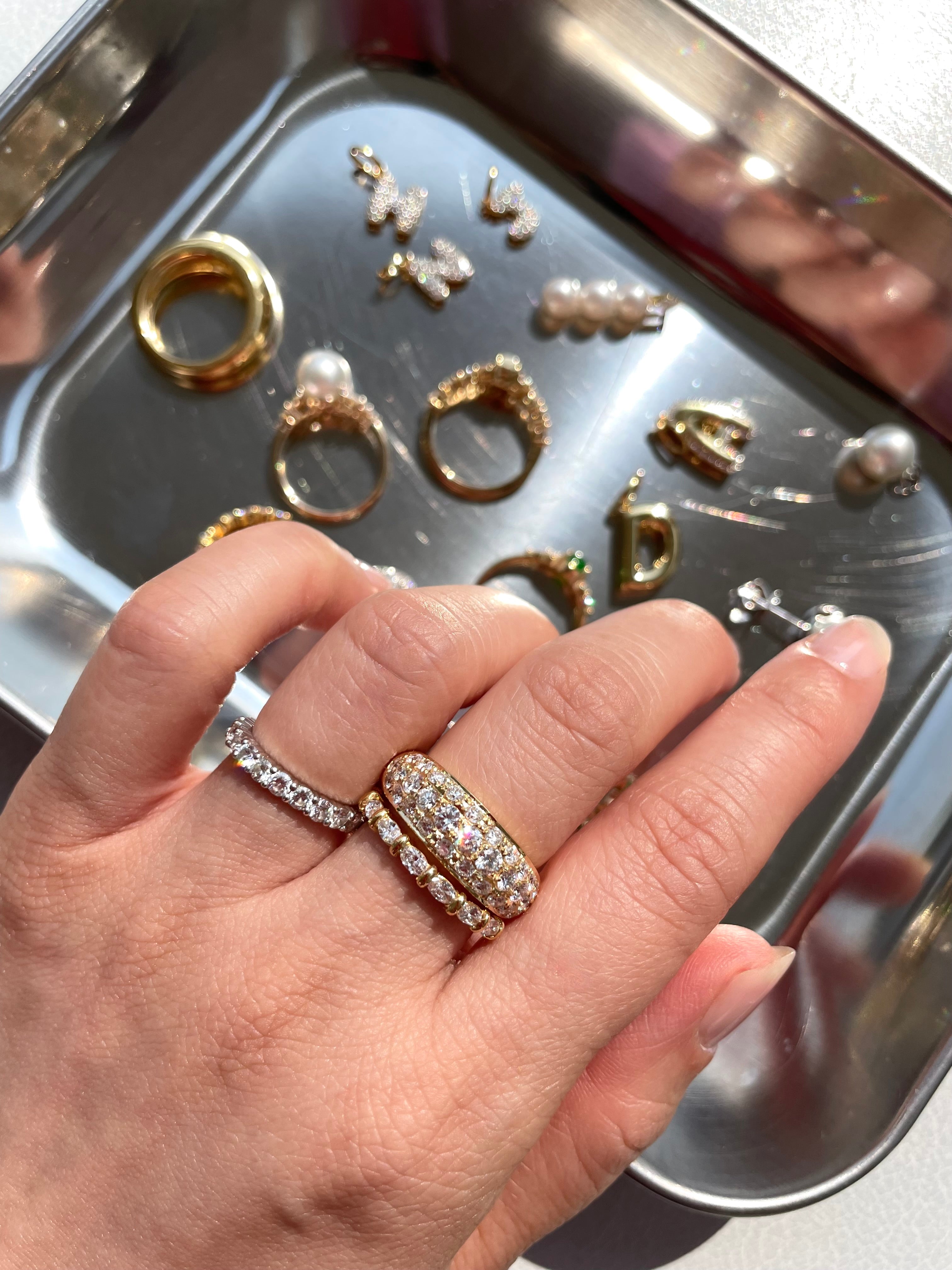 Hand wearing a diamond ring with a tray of additional rings in the background