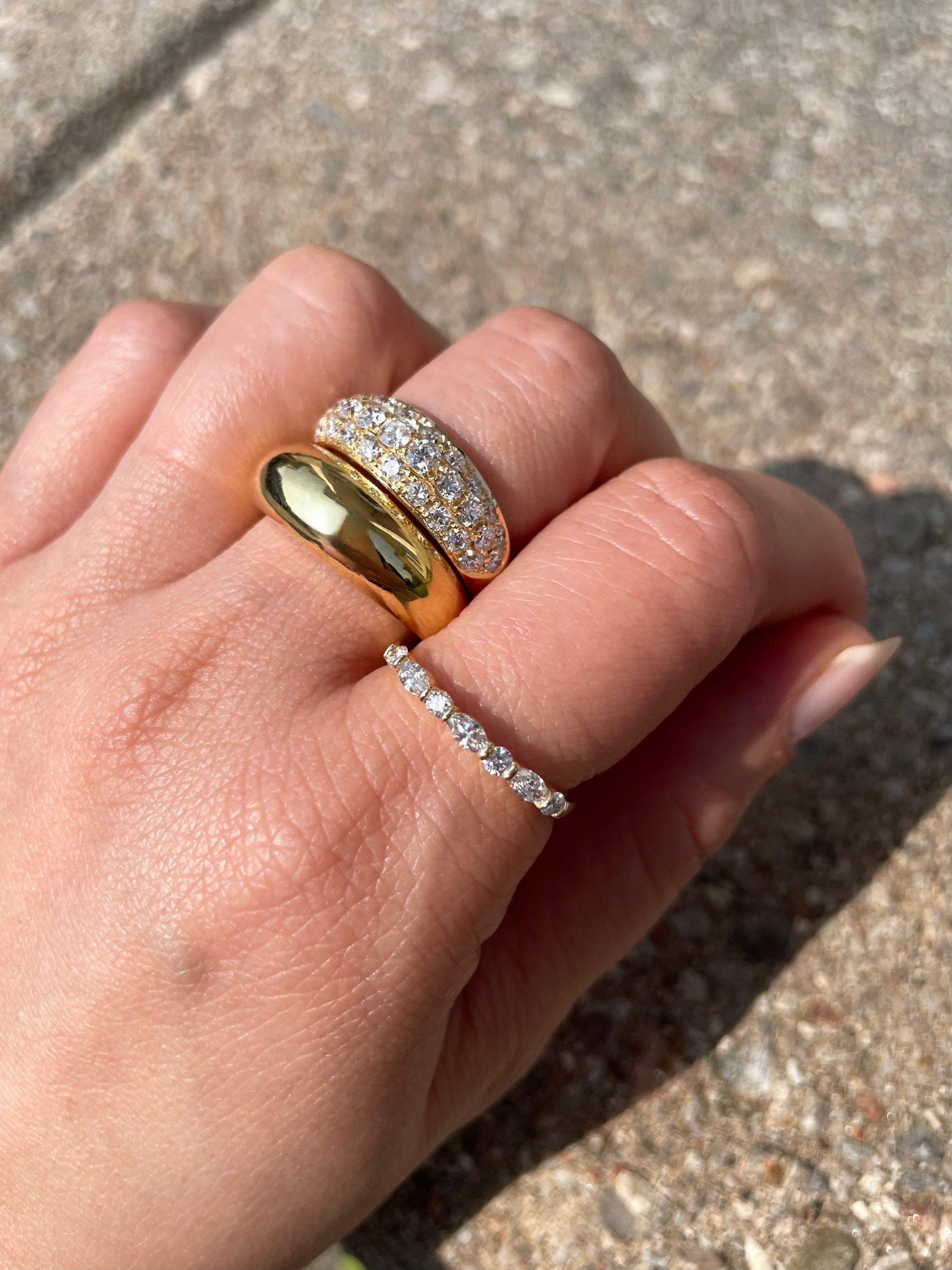 Hand wearing two gold rings with diamond accents on a concrete surface