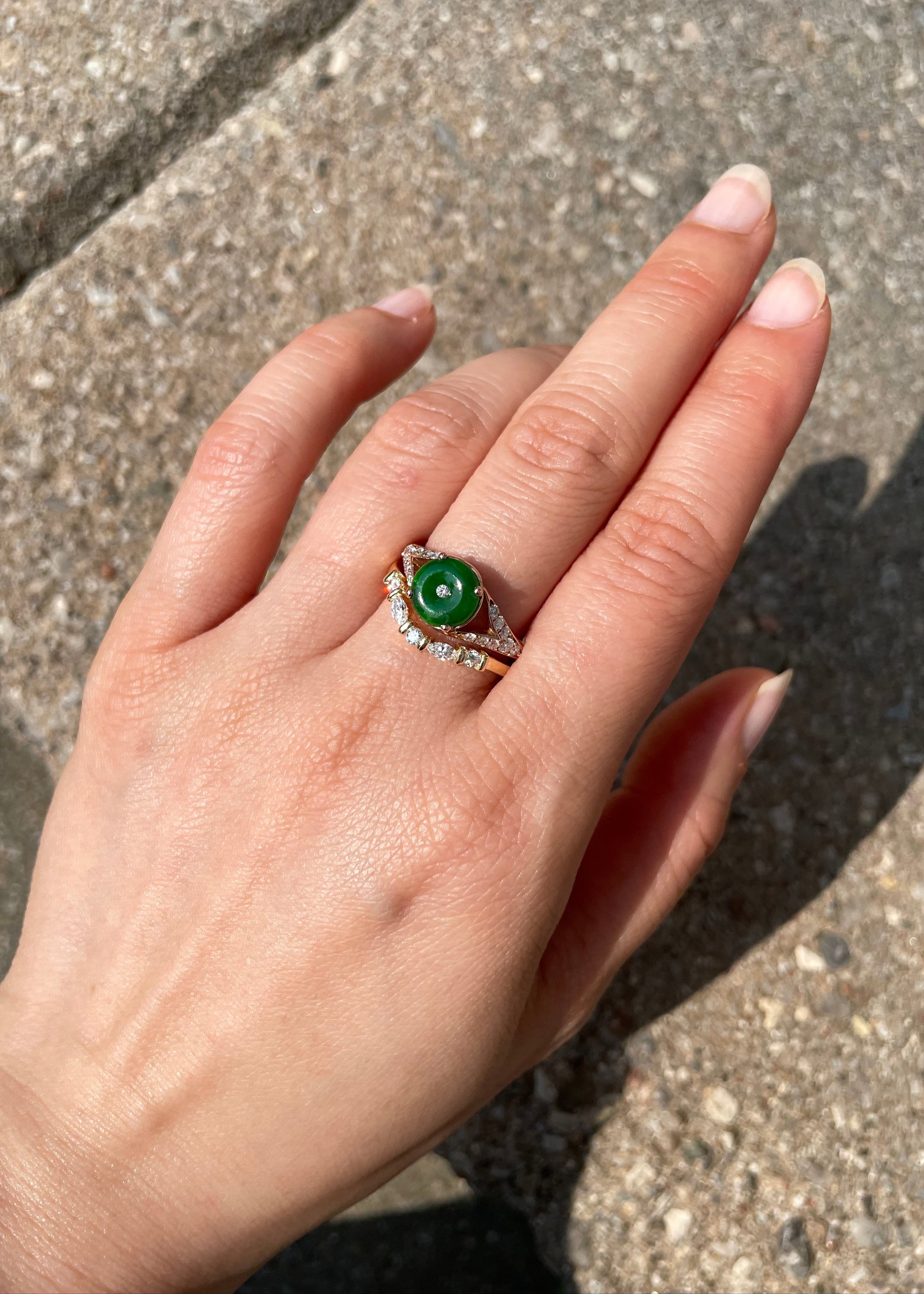Hand wearing a ring with a green gemstone on a concrete surface
