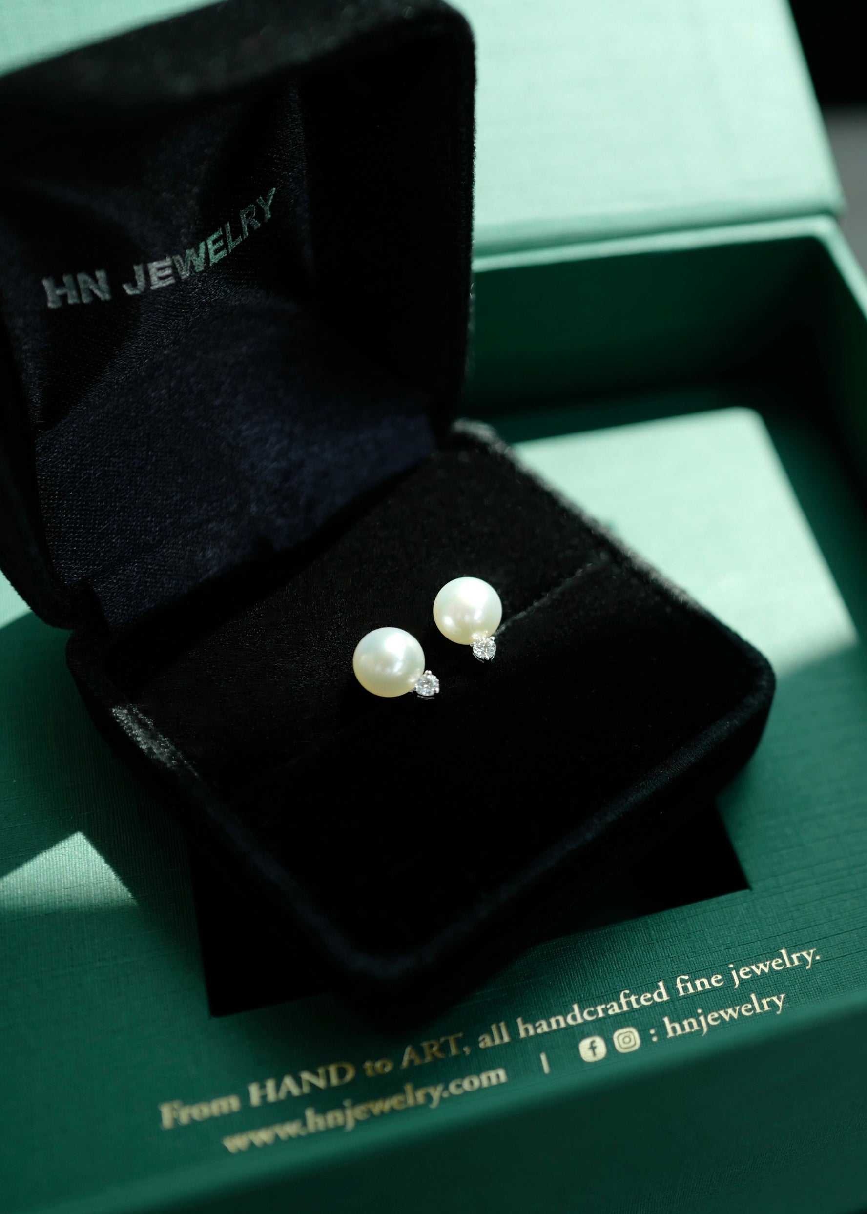 Pearl earrings in a black jewelry box on a green HN Jewelry branded box.