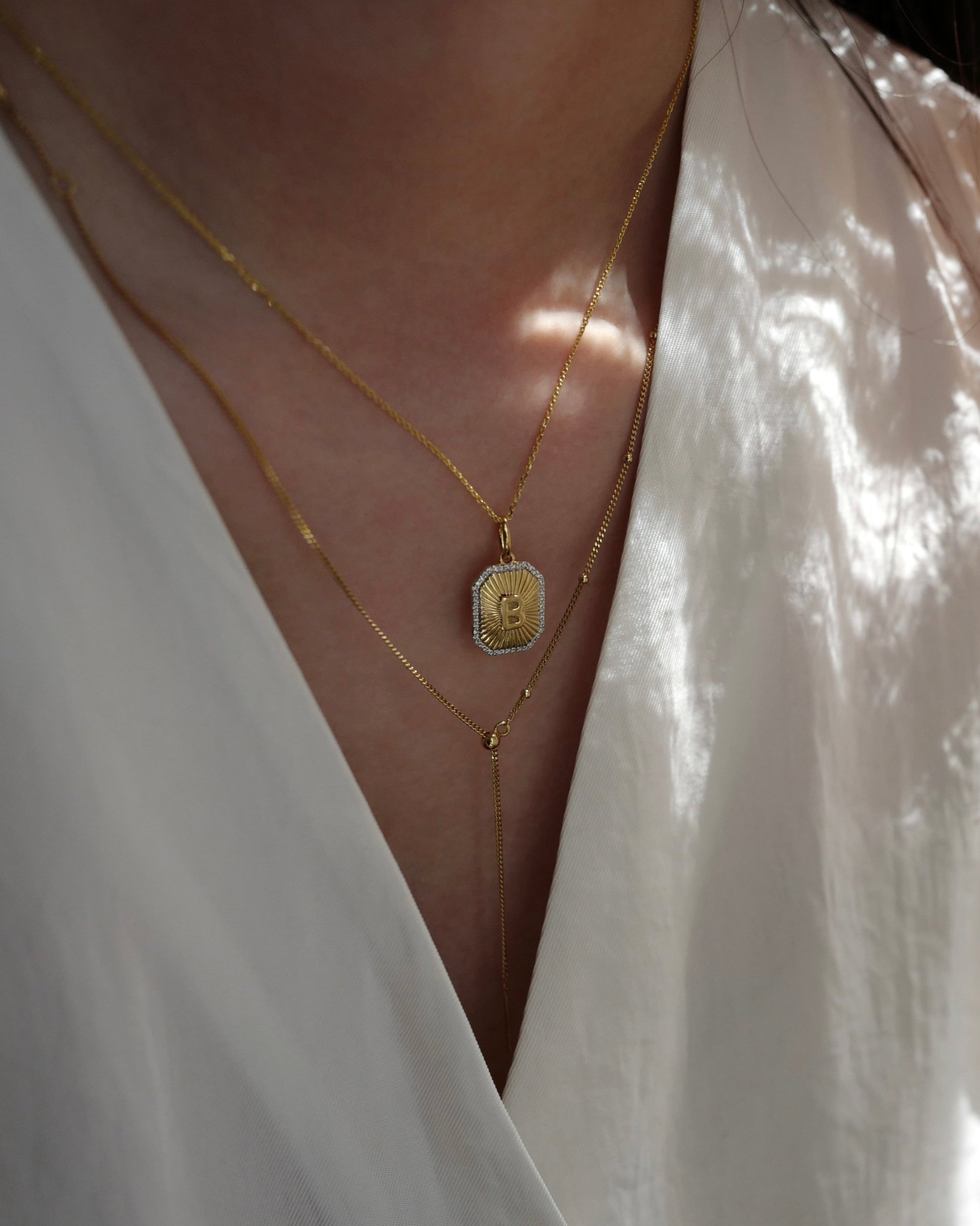 Close-up of a person wearing a gold necklace with a pendant against a white background