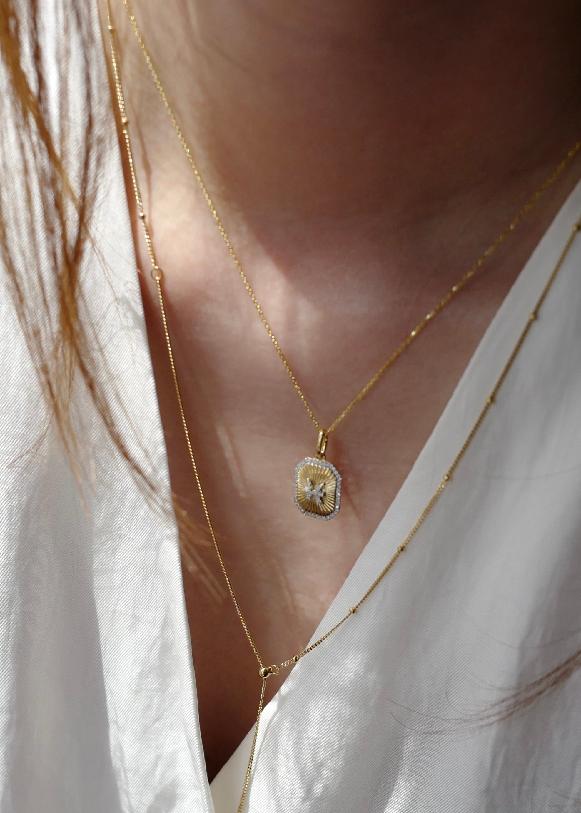 Close-up of a person wearing a gold necklace with a pendant on a white shirt.