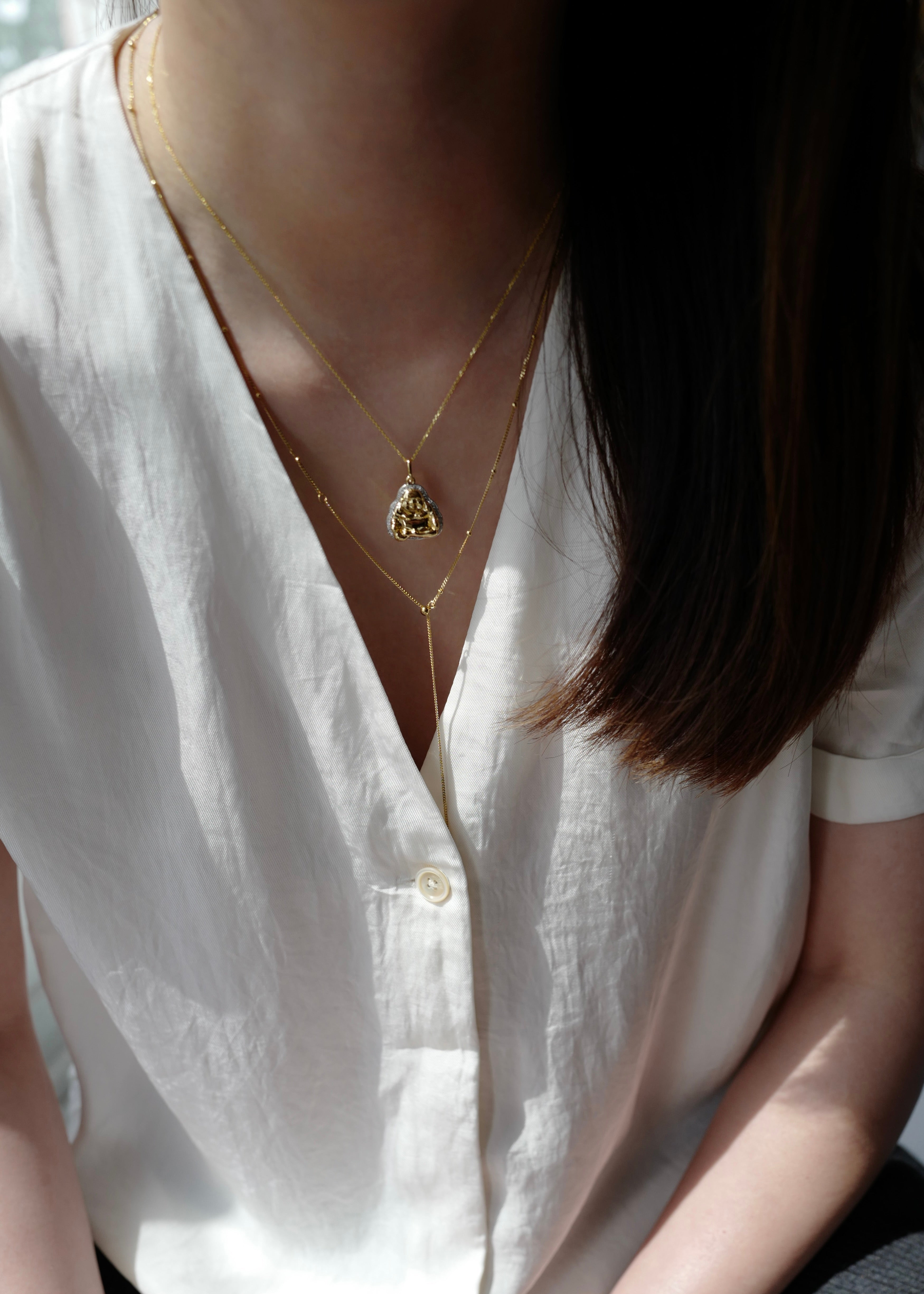 Person wearing a white shirt and gold necklace with a pendant.