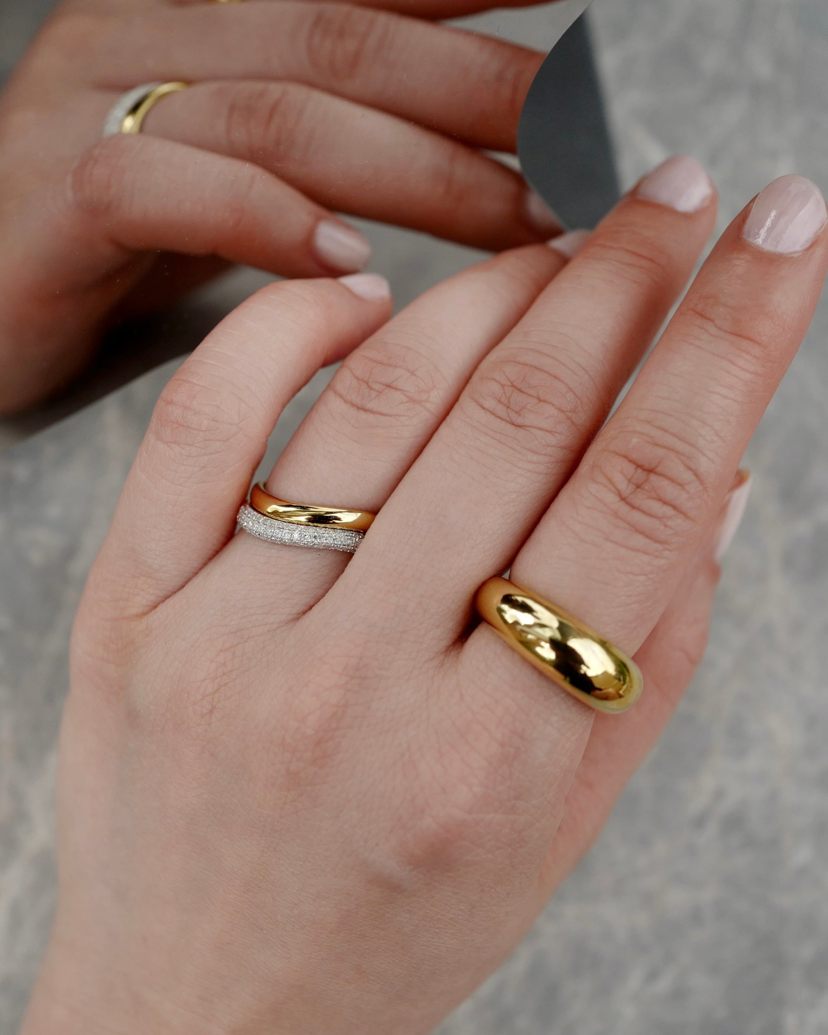 Close-up of hands wearing gold rings on a neutral background