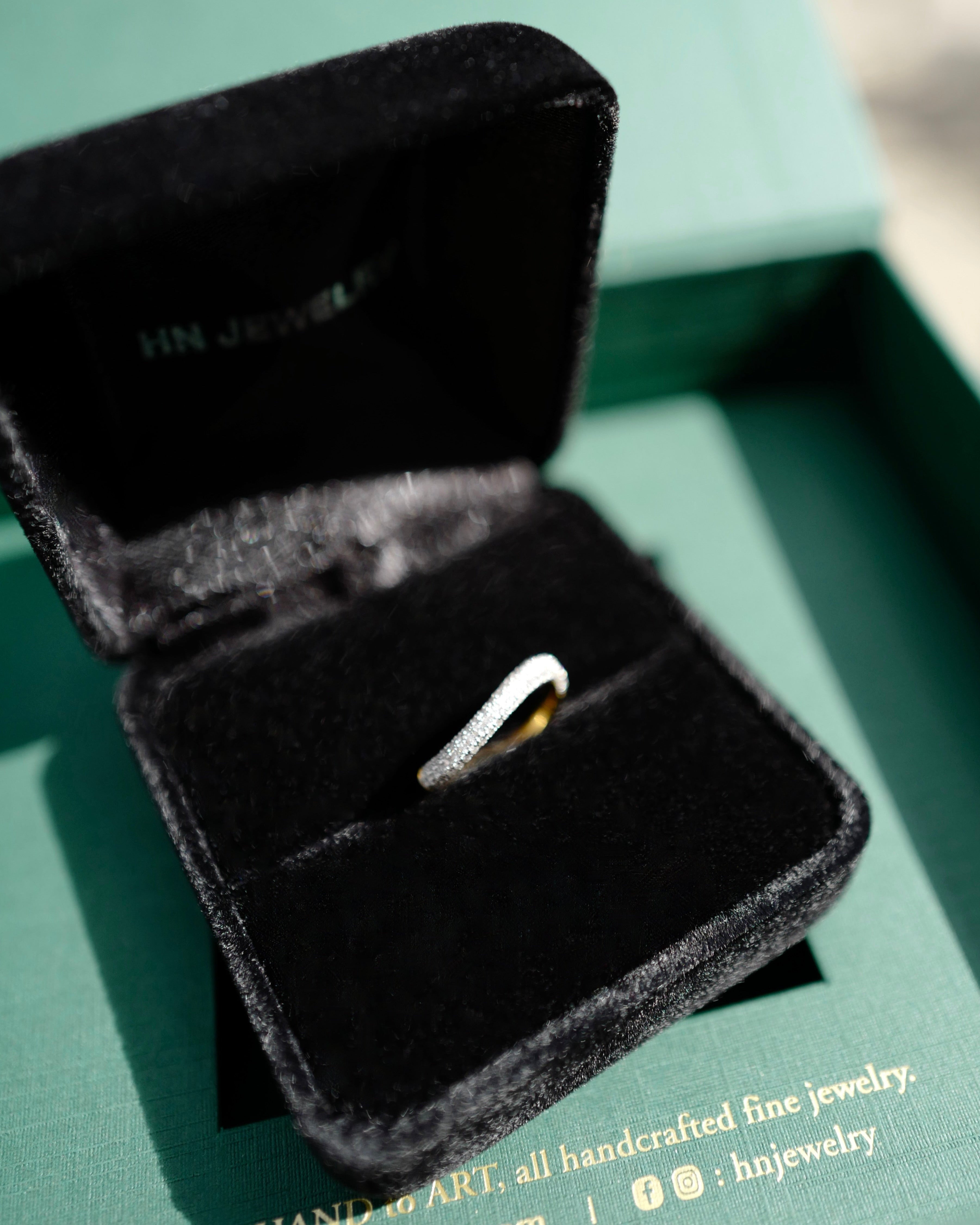 Gold ring in a black jewelry box on a green surface with 'HN Jewelry' branding.