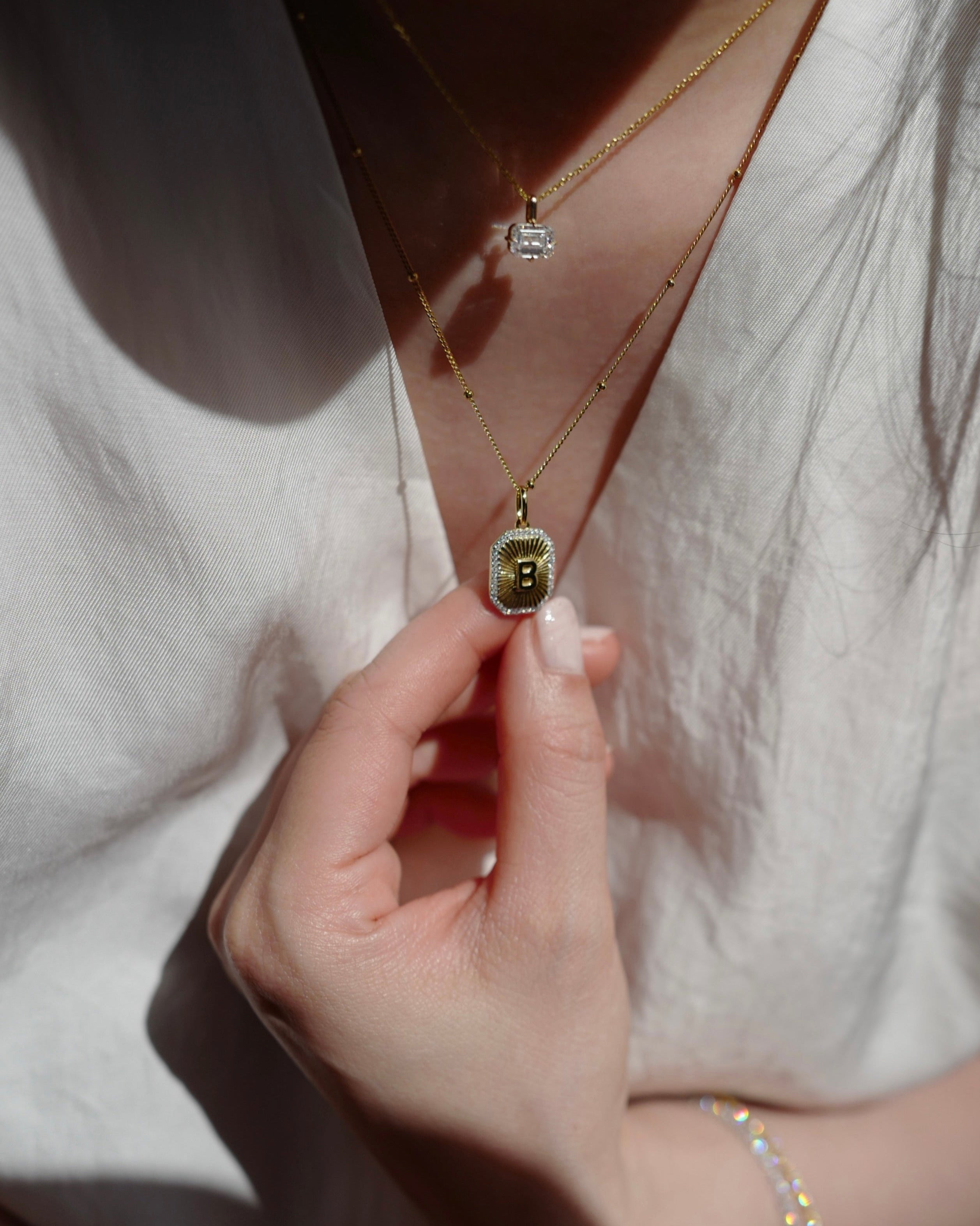 Close-up of a hand holding a gold necklace with a pendant against a neutral background