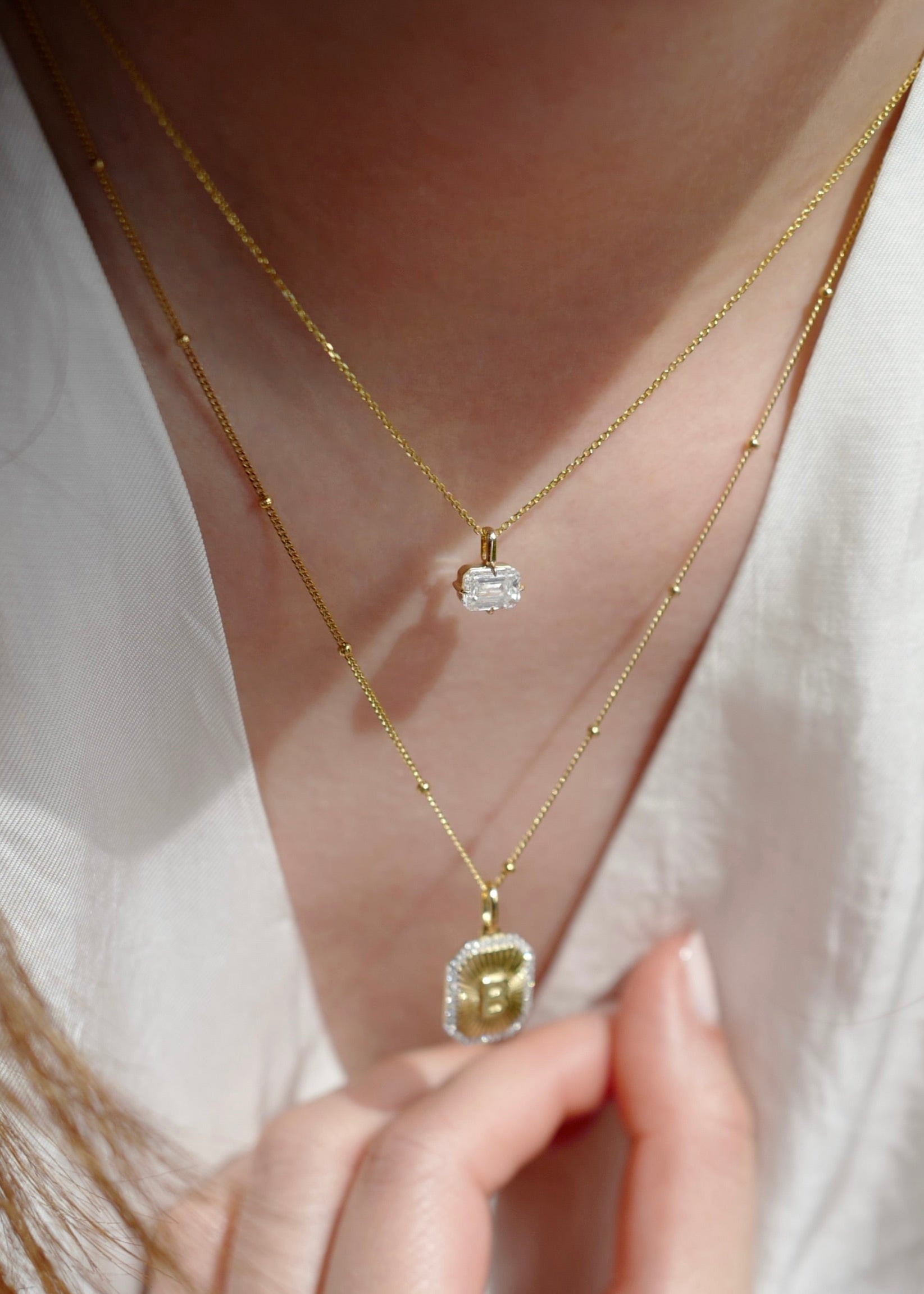Close-up of a person wearing two gold necklaces with pendants on a plain background