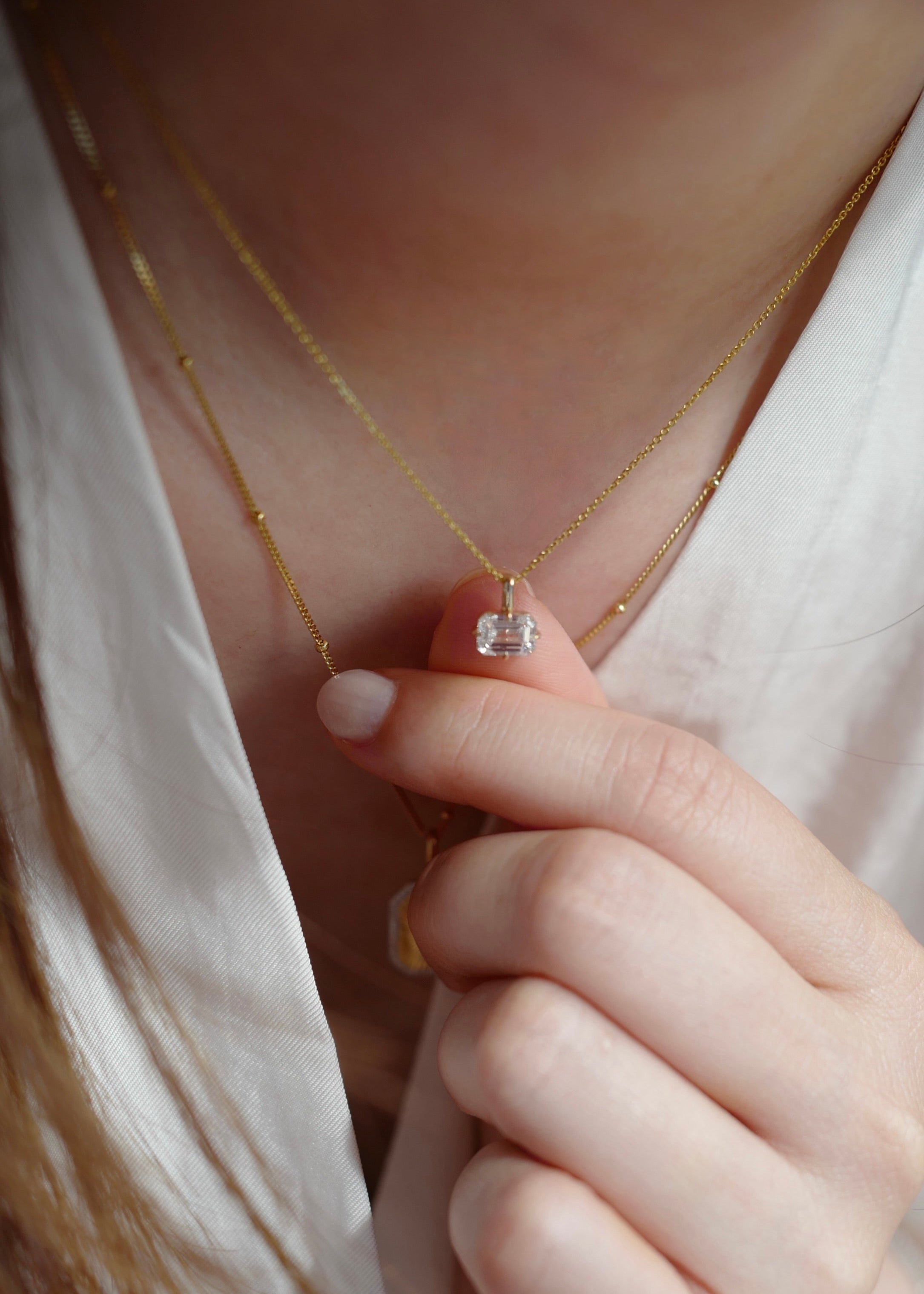 Gold necklace with a diamond pendant held by a hand against a soft background