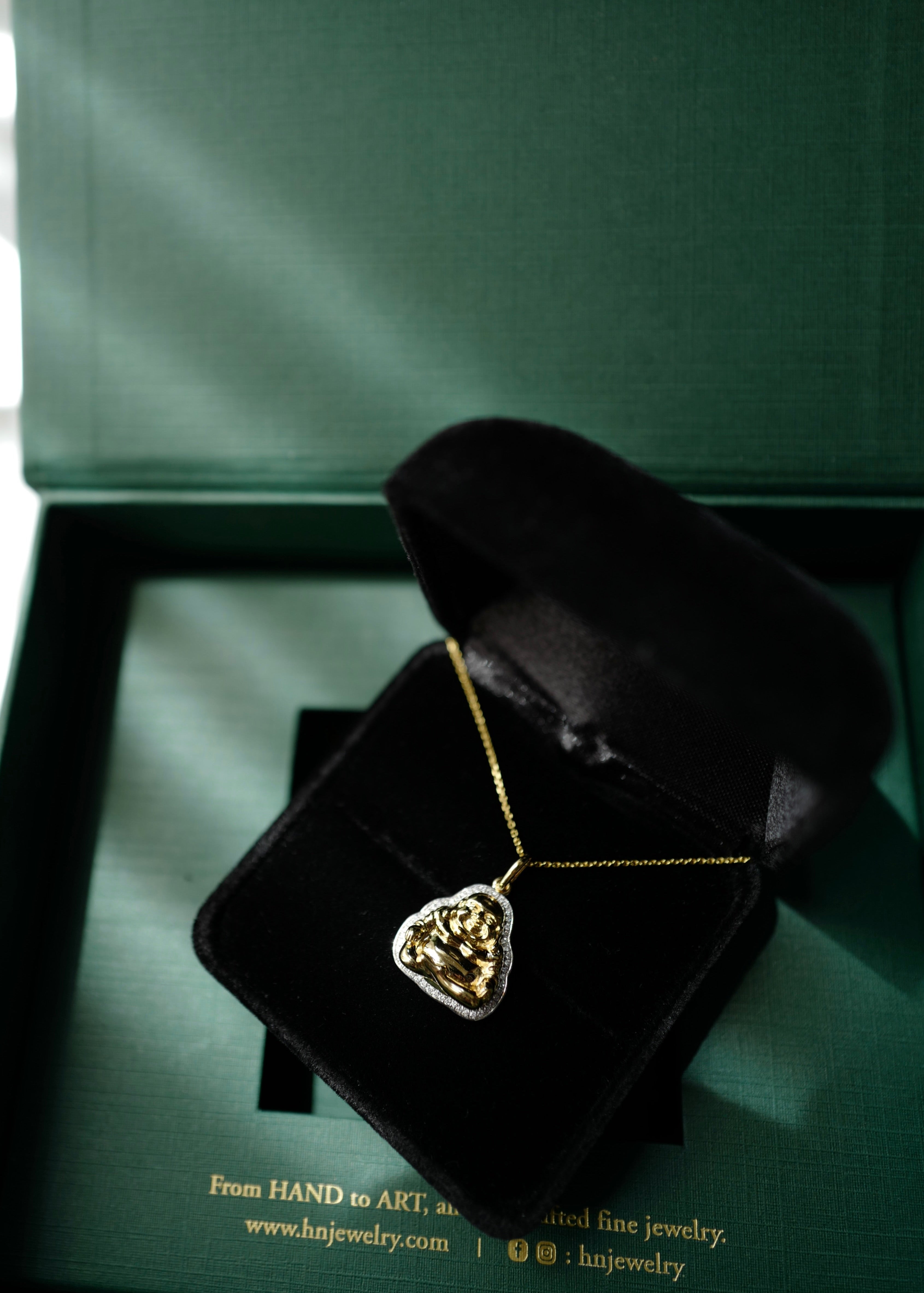 Gold necklace with a heart-shaped pendant on a black velvet stand with a green background.
