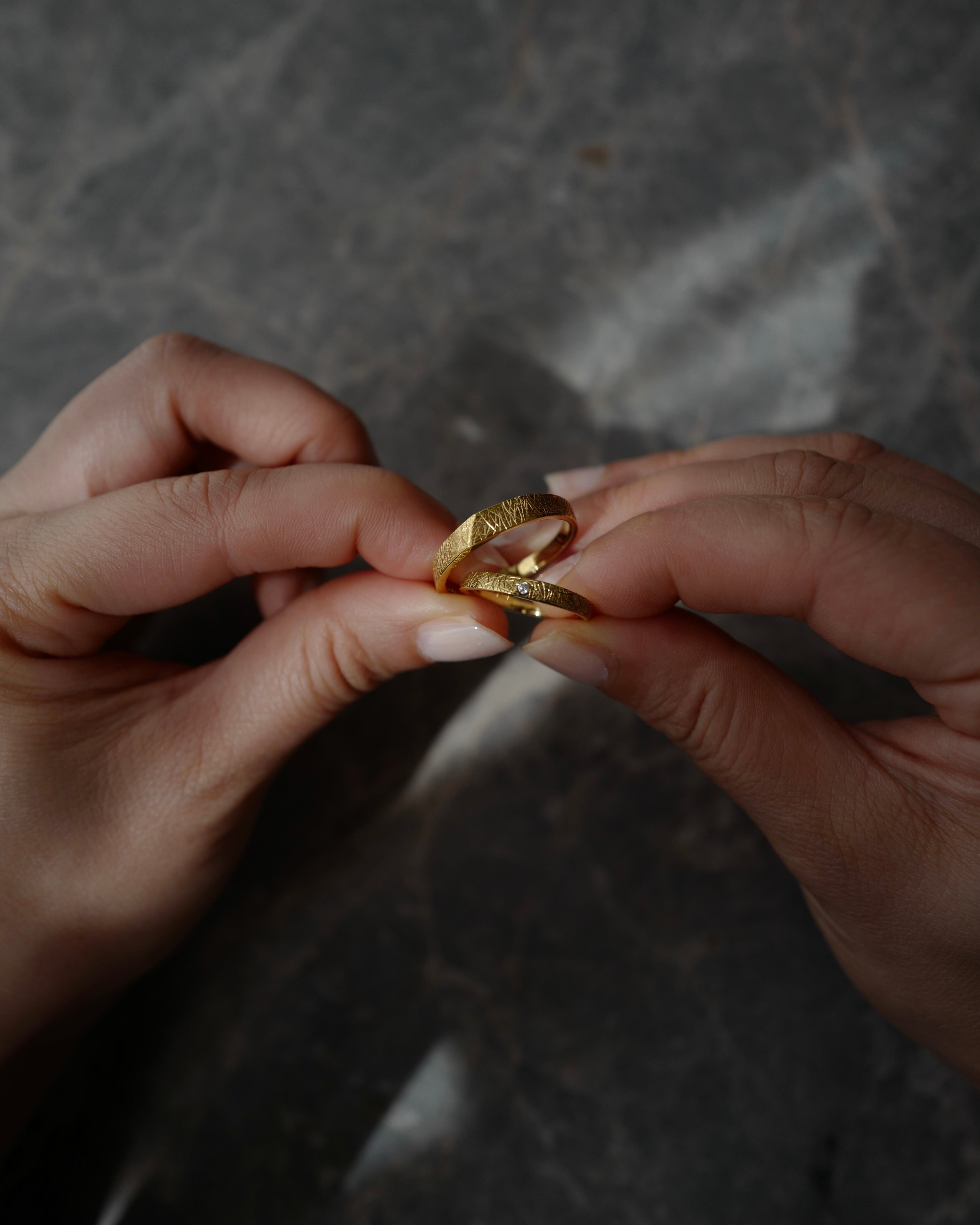 Close-up of hands holding a gold ring against a dark background