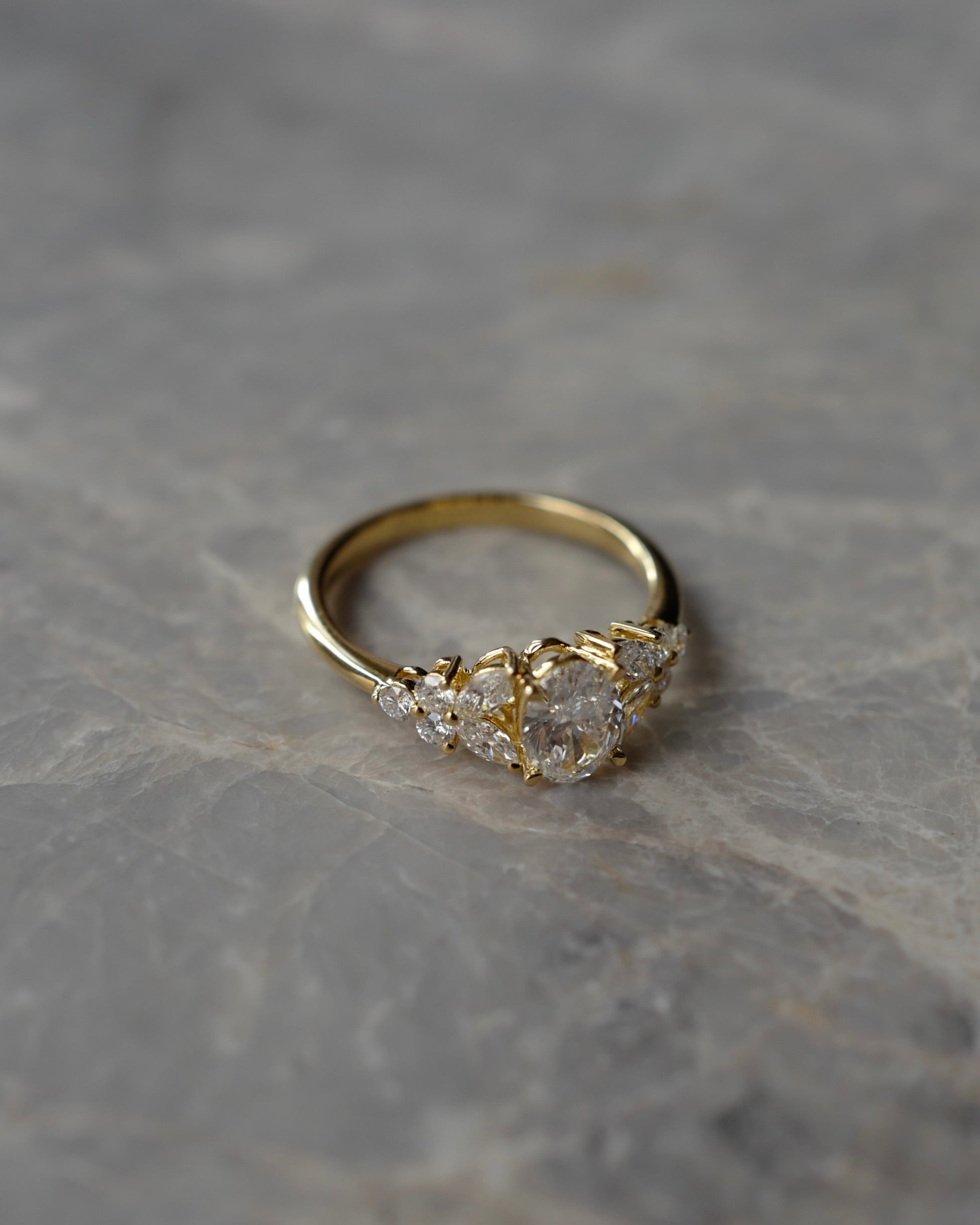 Gold ring with oval cut diamonds and marquise cut diamonds on a marble stone table. 