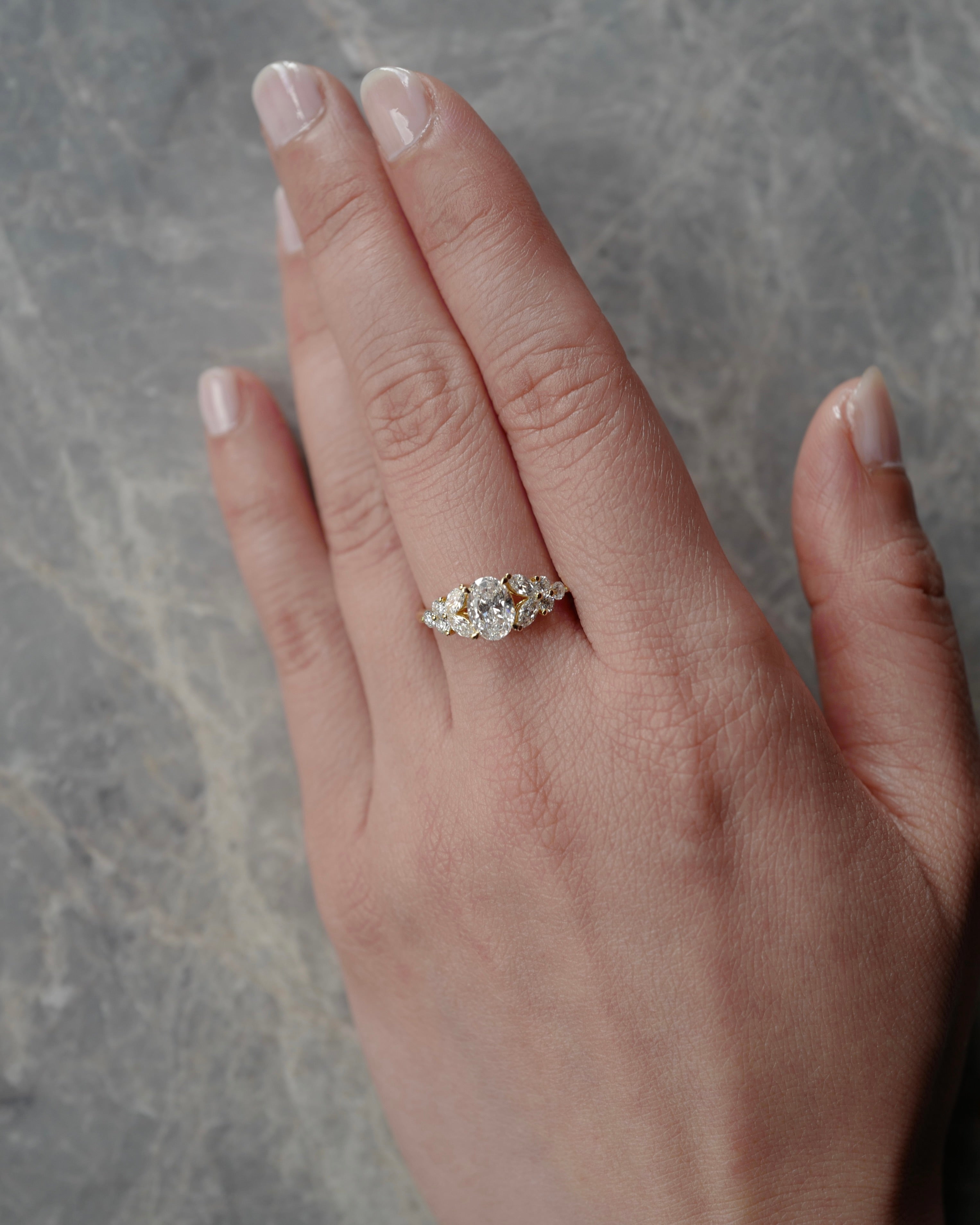 Hand wearing an oval cut diamond ring on a gray marble background