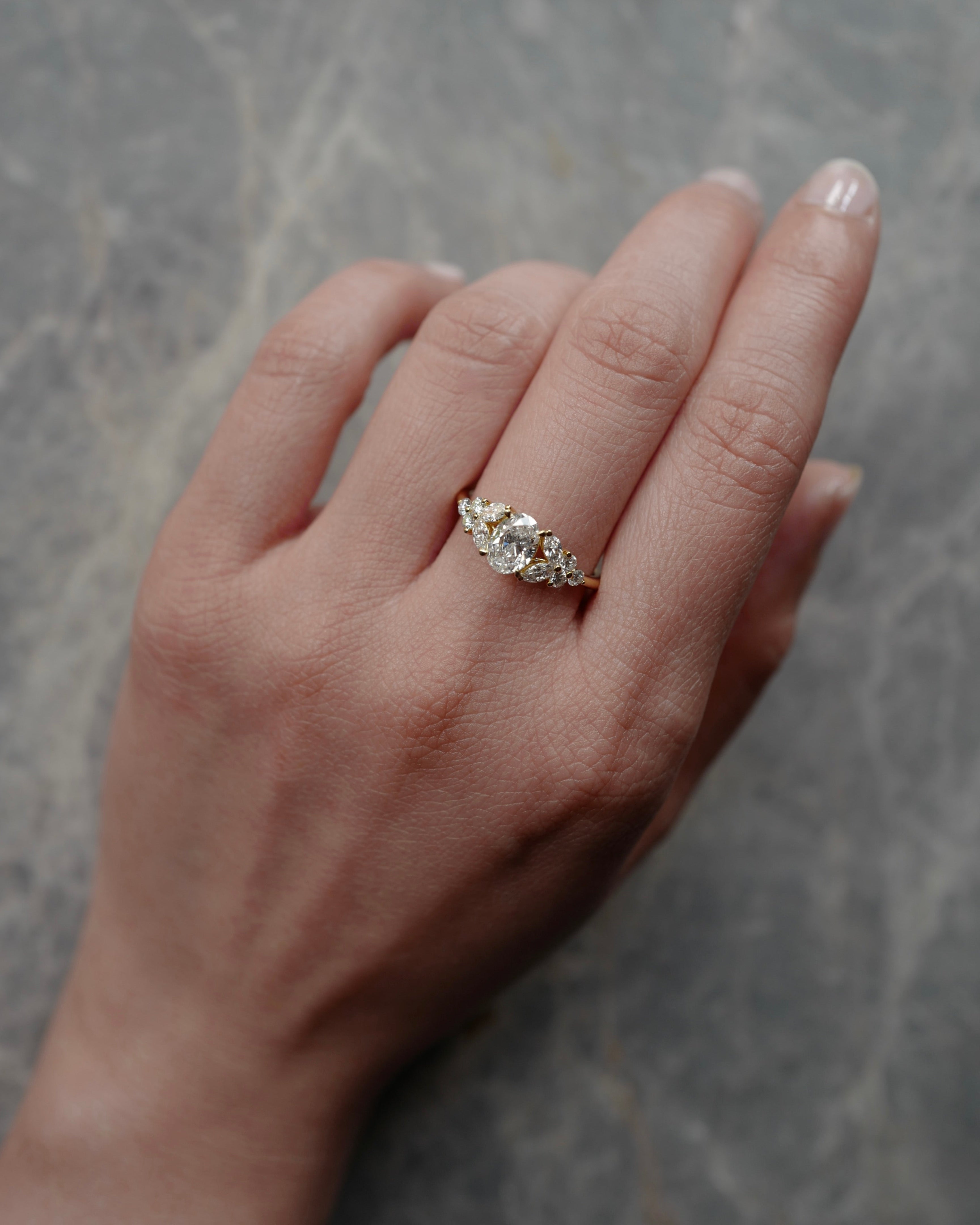 Hand wearing a oval cut diamond ring on a gray marble background